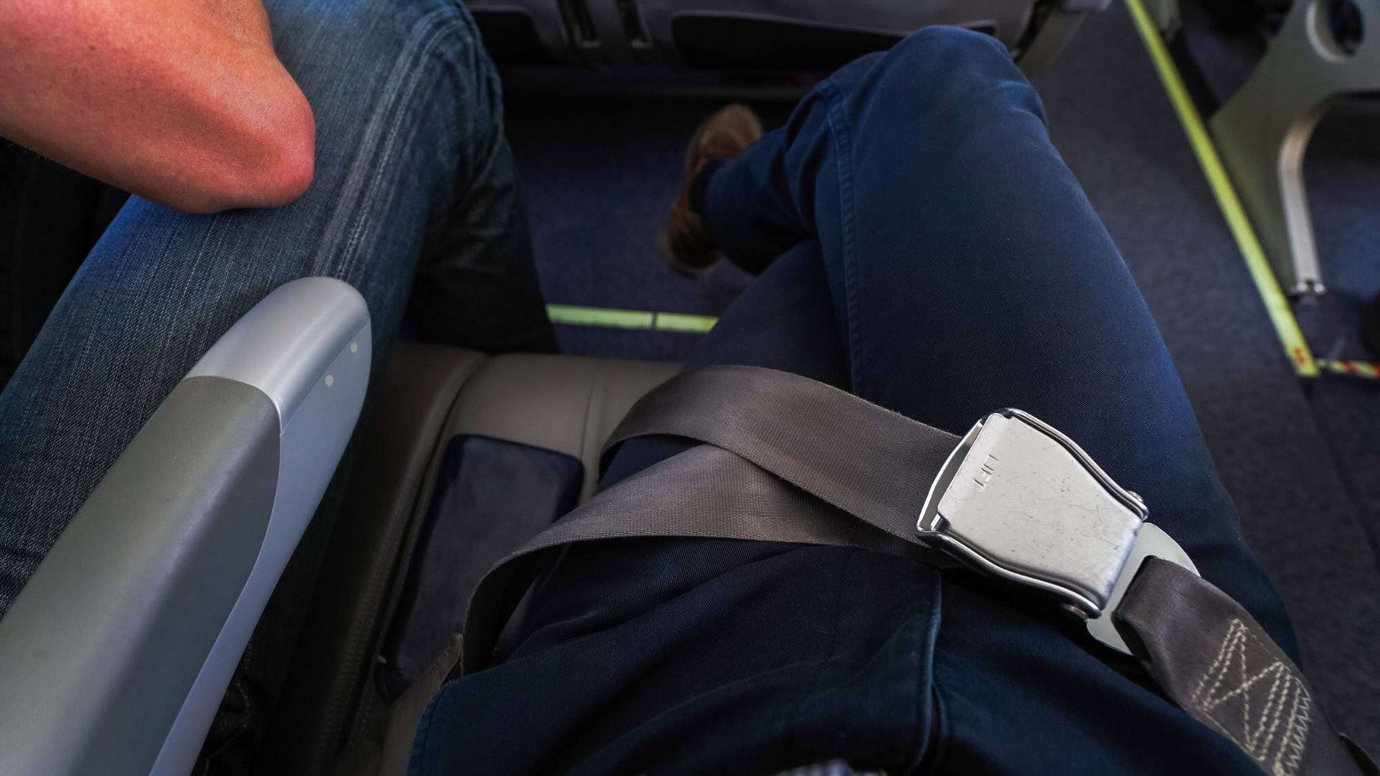 A view from above of a passenger’s lap with seatbelt fastened, showing cramped legroom and narrow seating space in economy class.