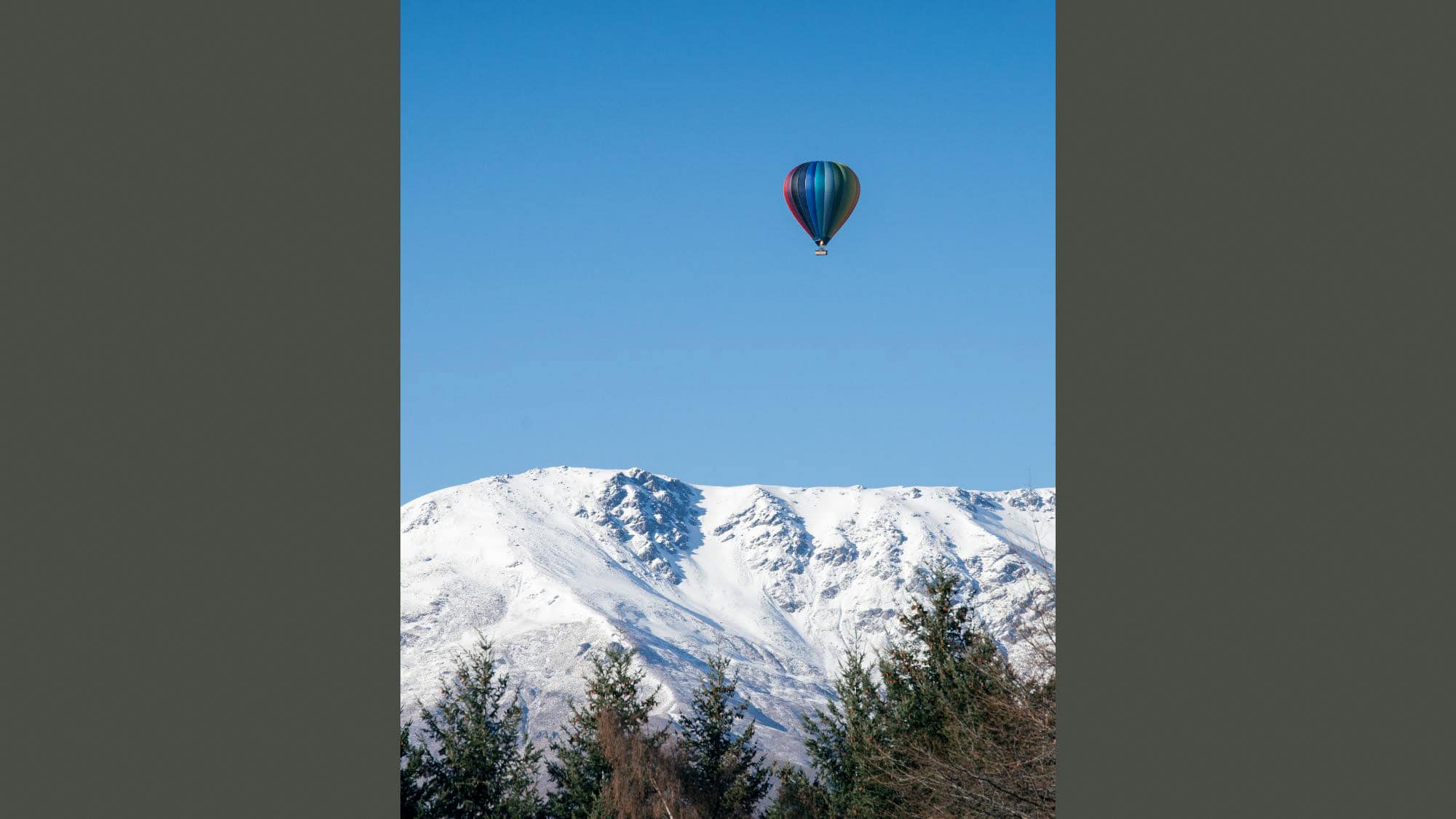 A hot air balloon floats over the snowy mountaintops near Queensland, New Zealand. 