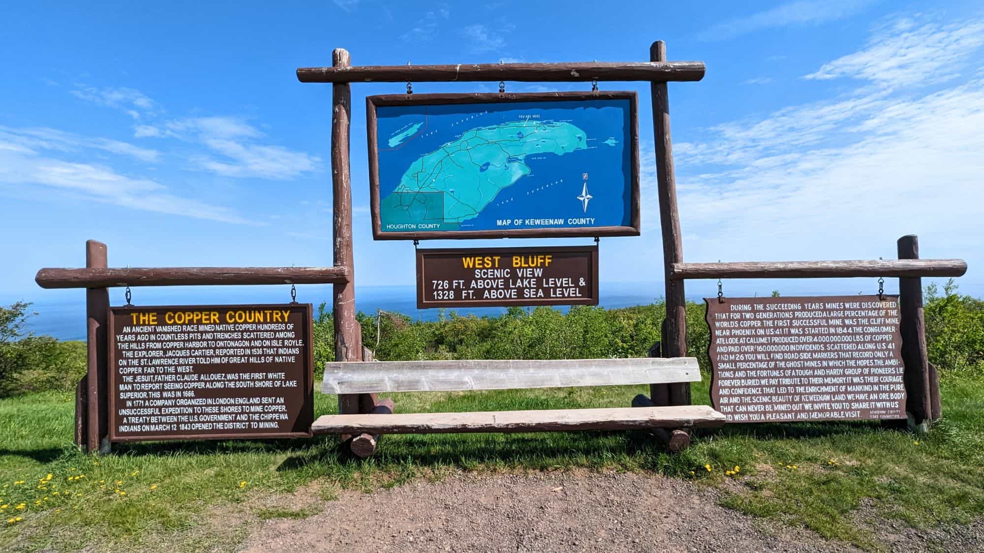 An informational sign at West Bluff overlooks Lake Superior, featuring a large map of Michigan’s Keweenaw Peninsula and historical panels about Copper Country mining.