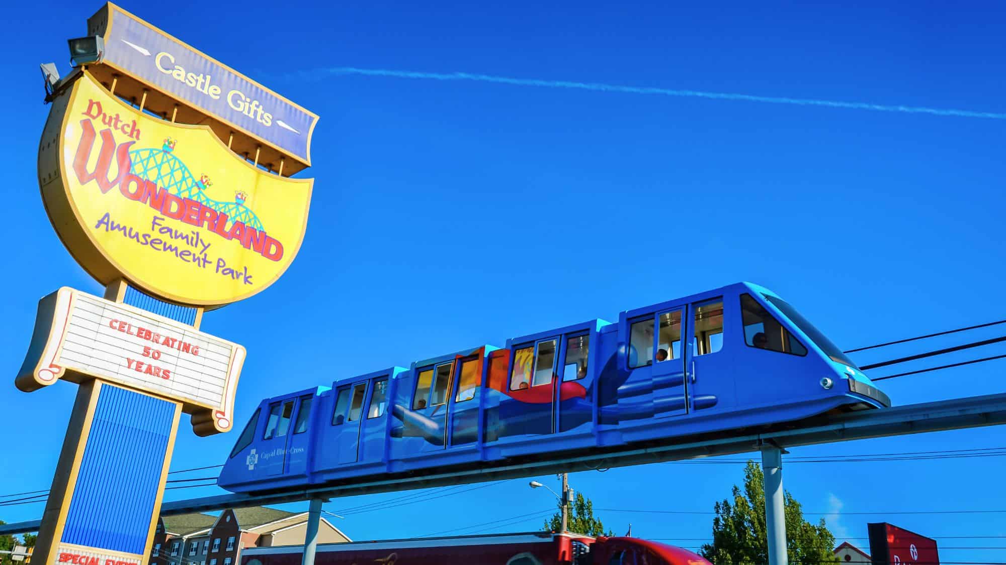 A colorful monorail glides past a large yellow Dutch Wonderland sign celebrating 50 years, set against a clear blue sky.