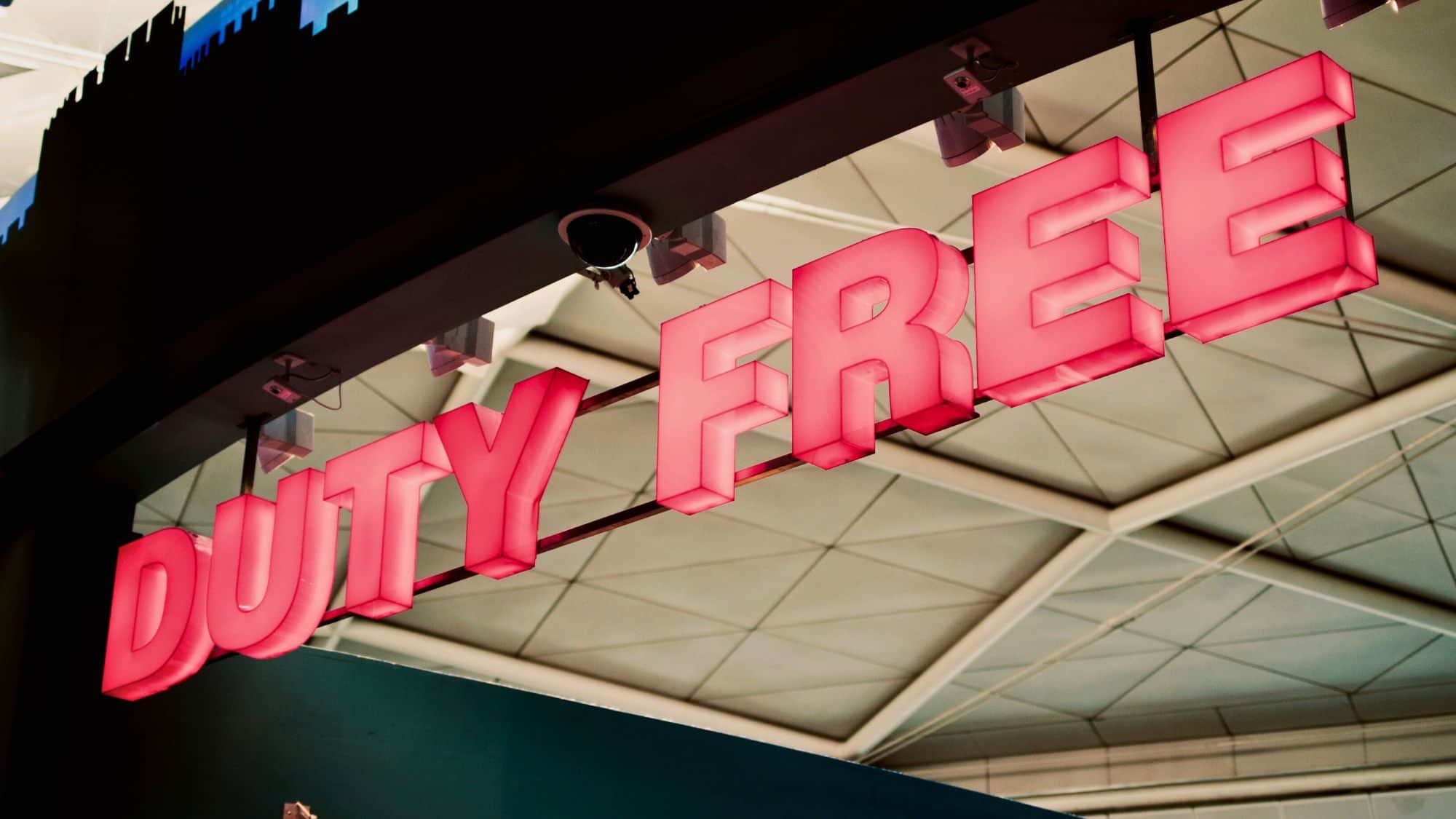 A bright pink neon “DUTY FREE” sign glows overhead, likely in a shopping area of a cruise terminal or onboard retail space.