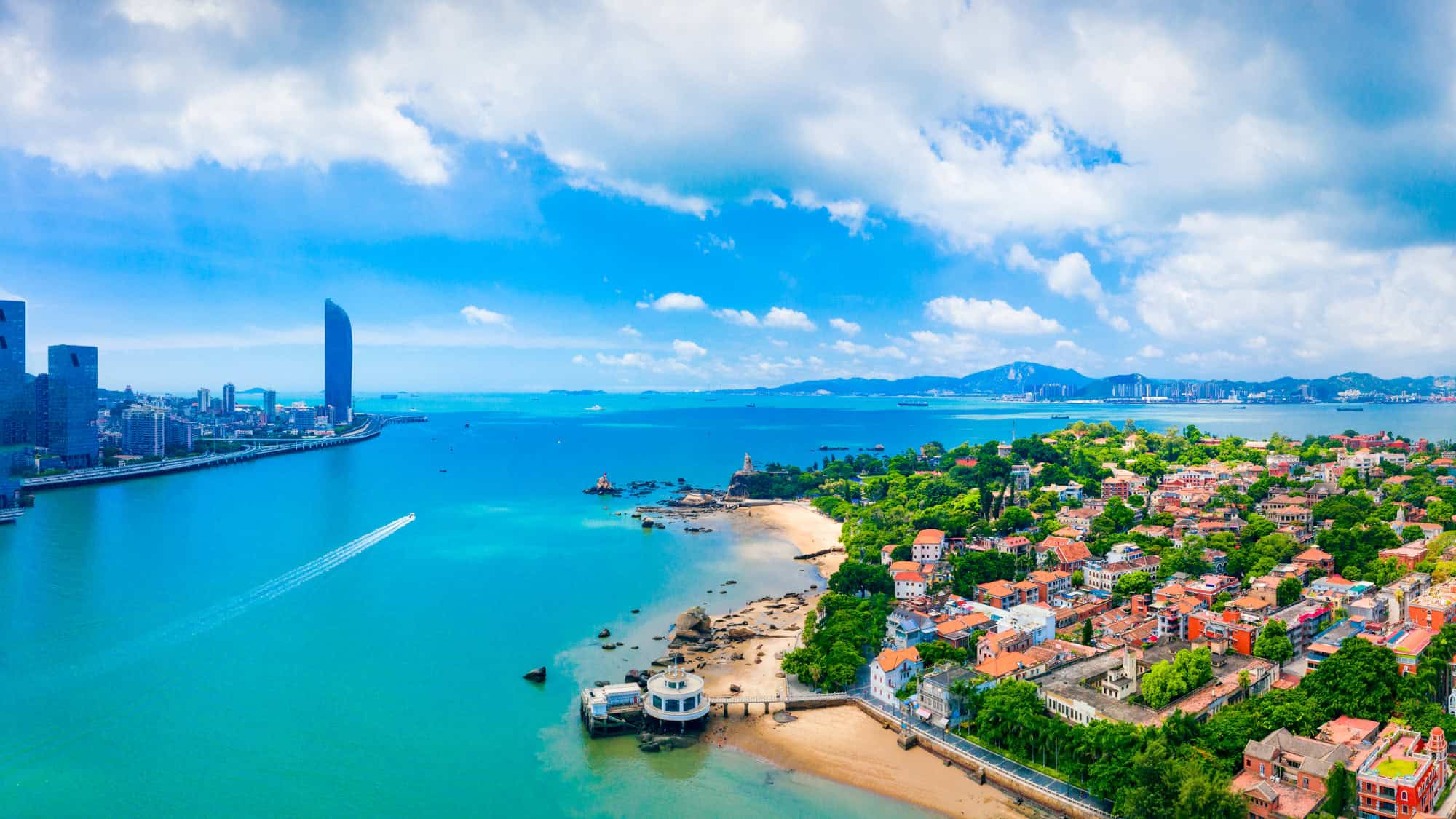 Aerial view of Xiamen, China, showcasing the contrast between modern skyscrapers on the mainland and the historic architecture and beaches of Gulangyu Island.