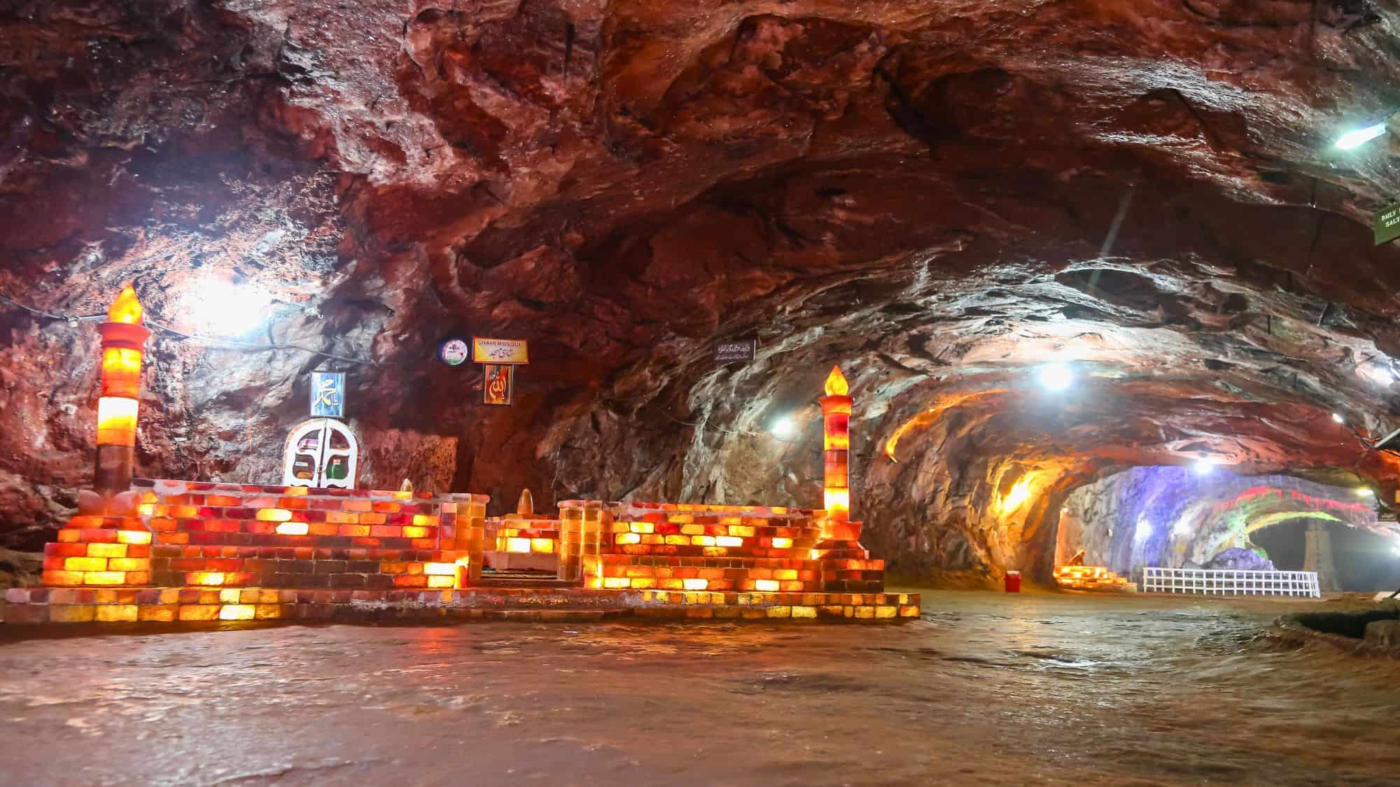 A glowing salt brick structure resembling a mosque stands within a red-hued salt cave, decorated with small banners and warm lights.
