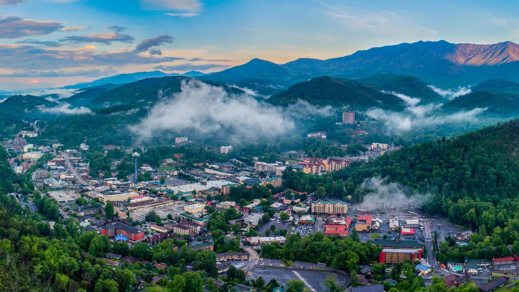 Low fog drifts between forested ridges surrounding Gatlinburg, Tennessee, as the mountain town’s buildings and roads nestle in the valley.