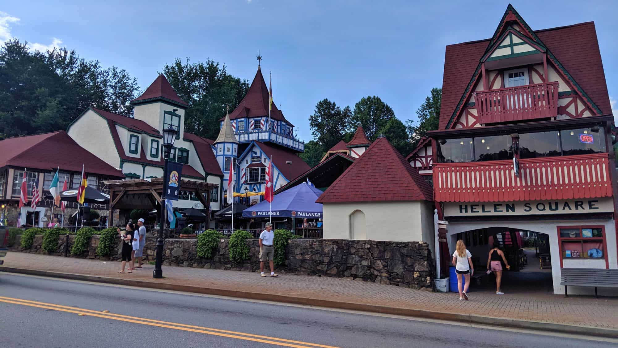 Colorful Bavarian-themed buildings with steep roofs and balconies line a cobbled street in Helen, Georgia, complete with international flags and open-air patios.