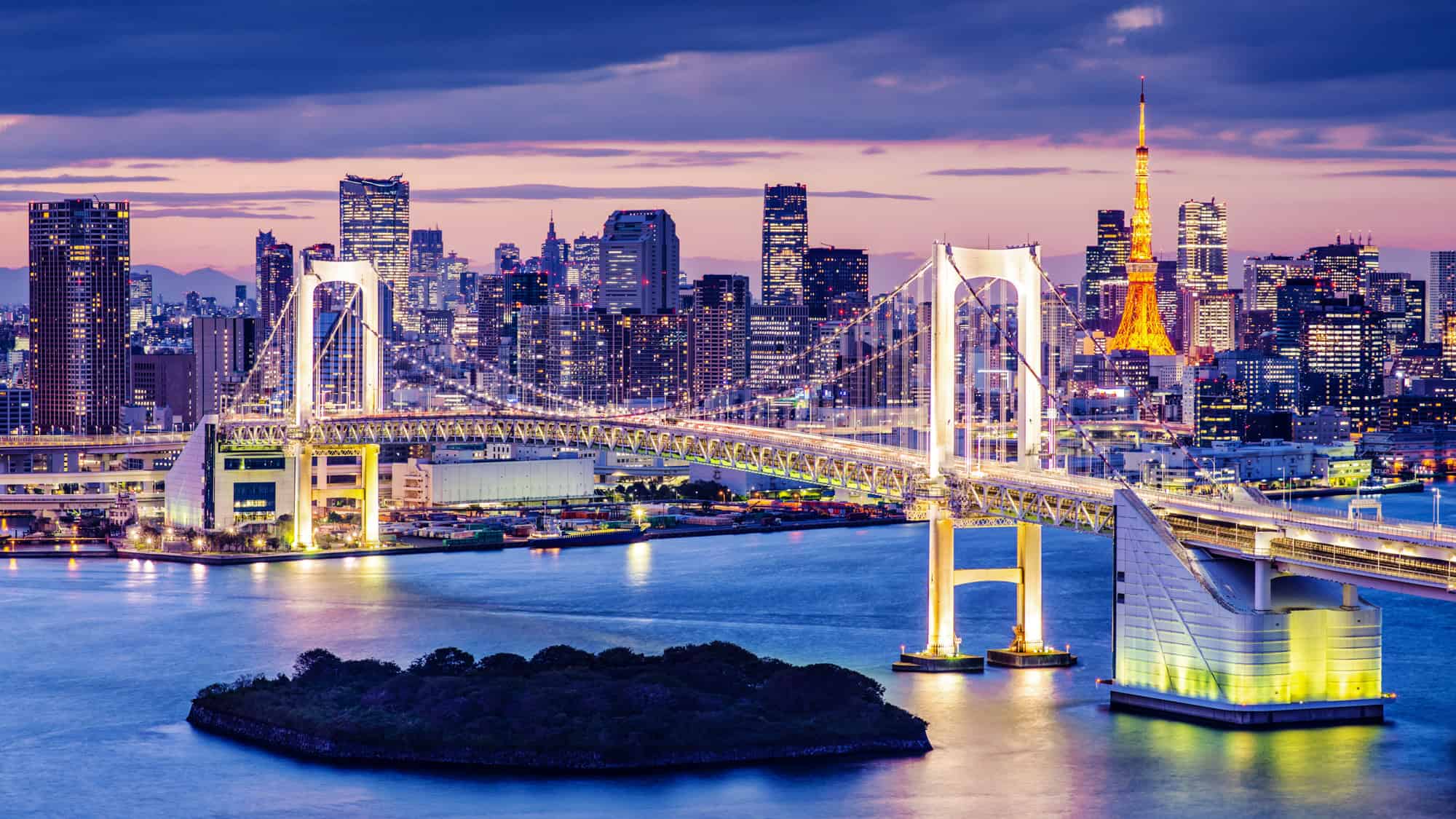 Tokyo’s Rainbow Bridge glows with white lights at twilight, spanning the bay with Tokyo Tower shining orange in the background against a pastel skyline.