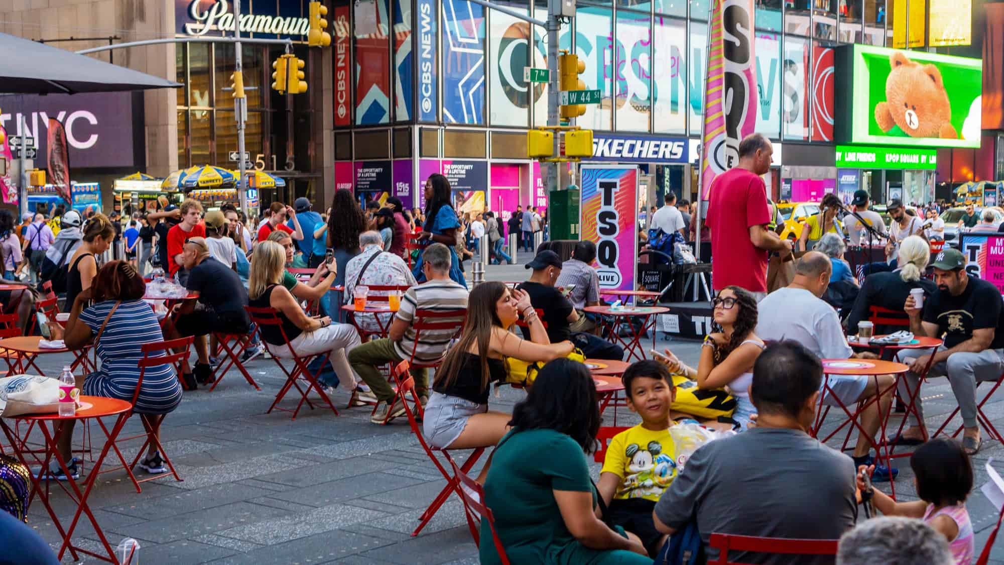 Neon billboards and LED screens light up the bustling heart of Times Square, where people gather among during a summer afternoon. 