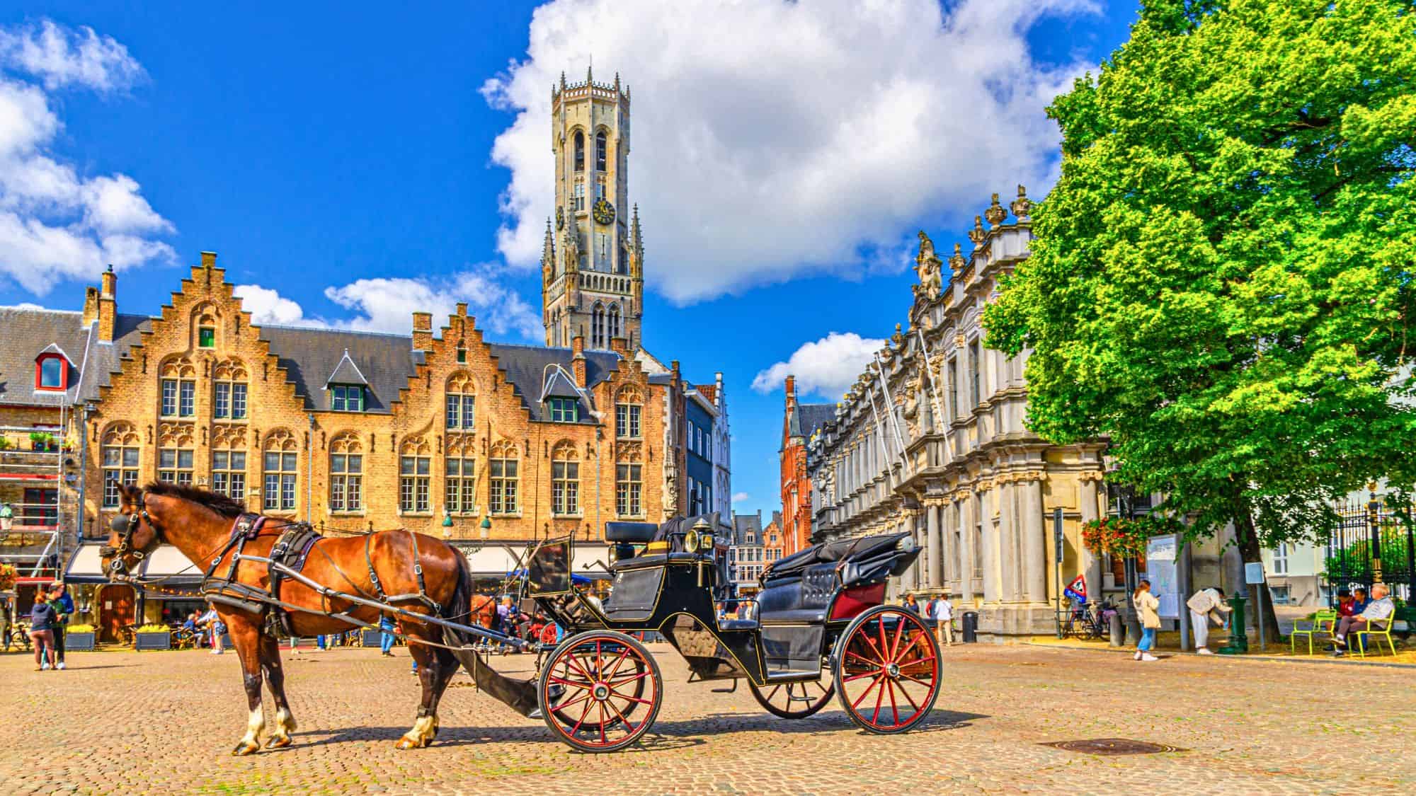 A horse-drawn carriage stands in Bruges’ historic market square, framed by medieval architecture and the iconic Belfry tower.