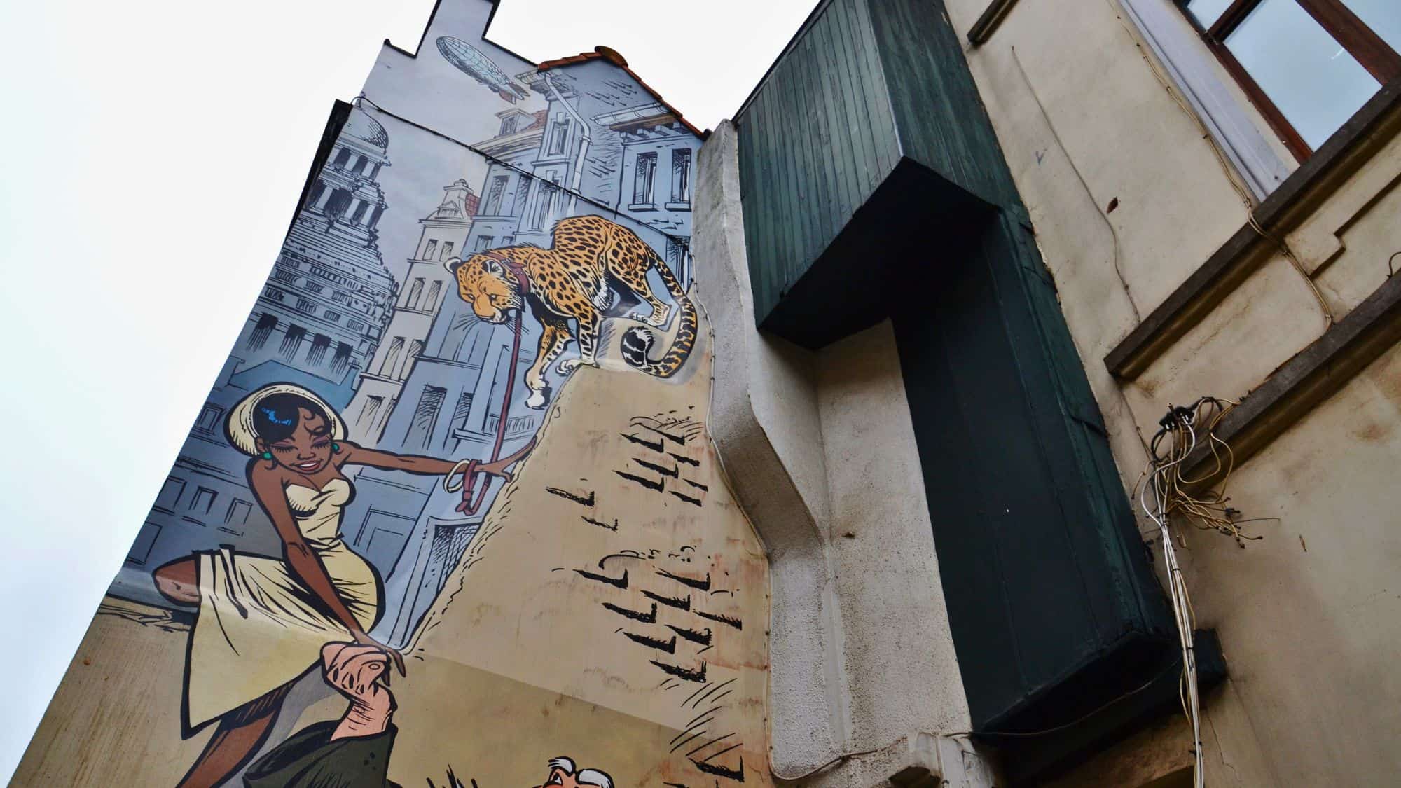 A vibrant mural on a city wall depicts a woman and a leopard in comic strip style, part of Brussels' famous comic art trail.