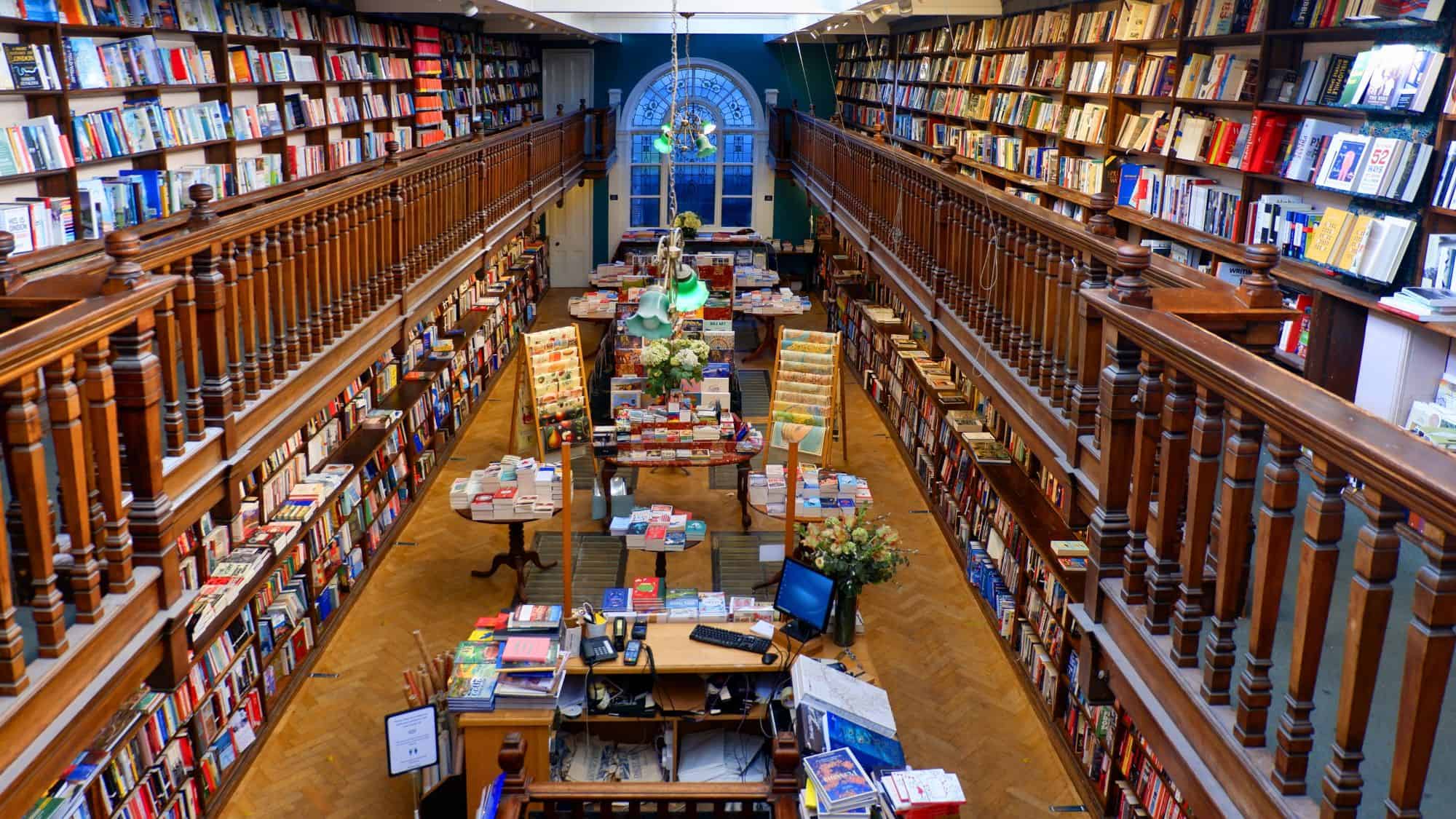 An elegant Edwardian bookshop with oak galleries and skylights, lined wall-to-wall with books and tables overflowing with colorful titles.