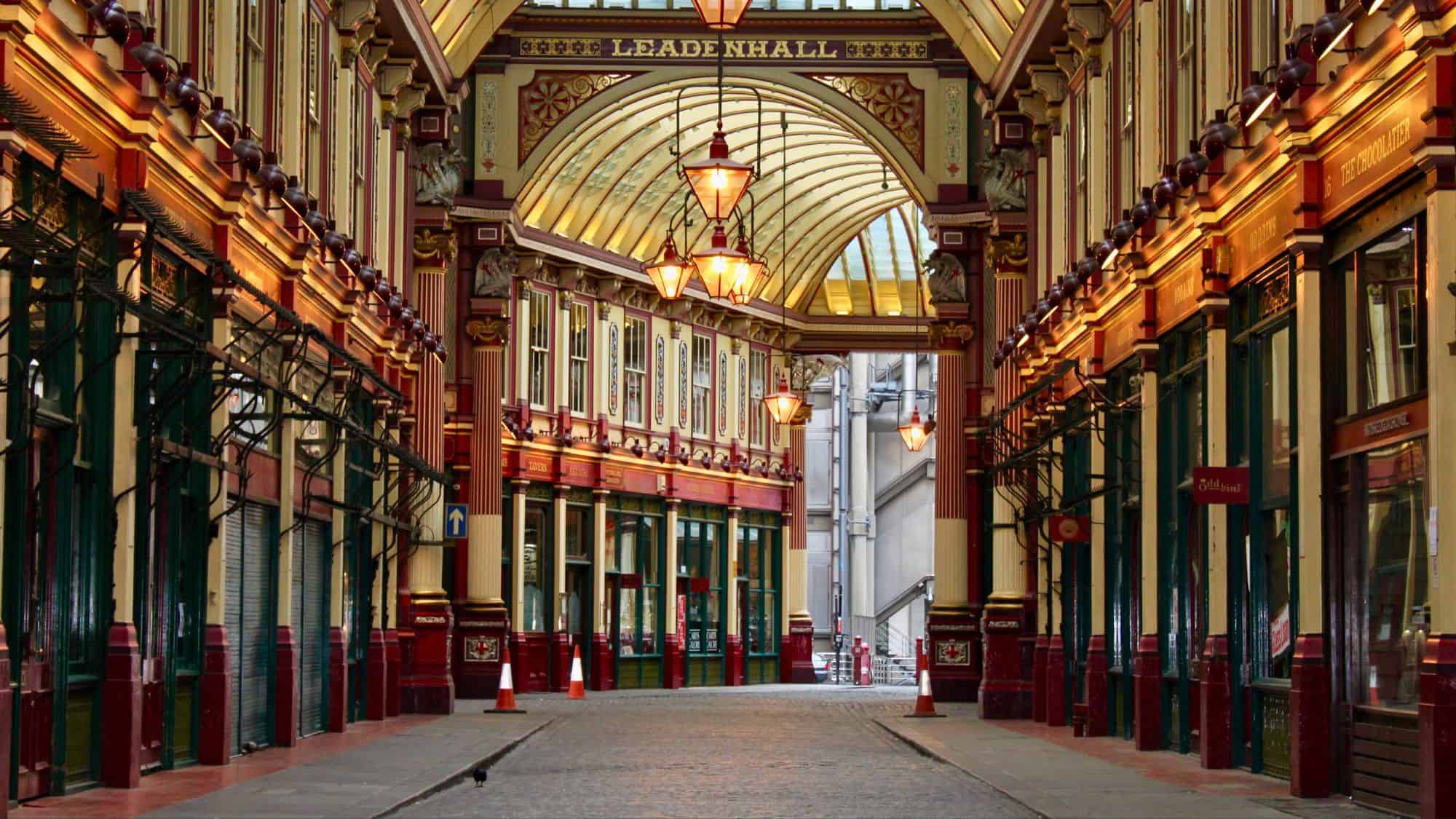 An elegant view down the main hall of Leadenhall Market, featuring intricate red-and-gold details, glass ceilings, and warm lamplight.