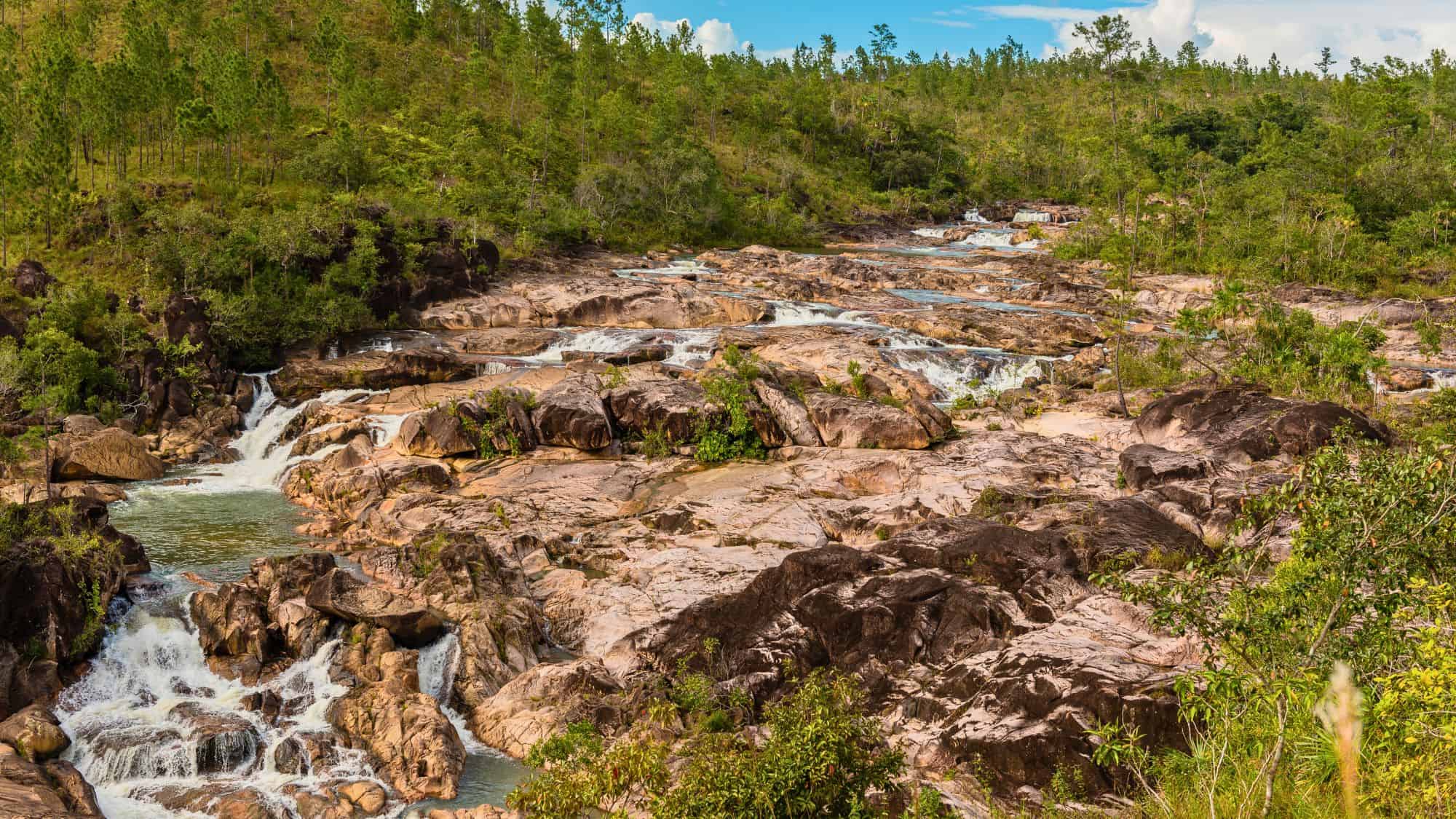 A series of natural rock pools and small waterfalls flowing through a forested landscape.