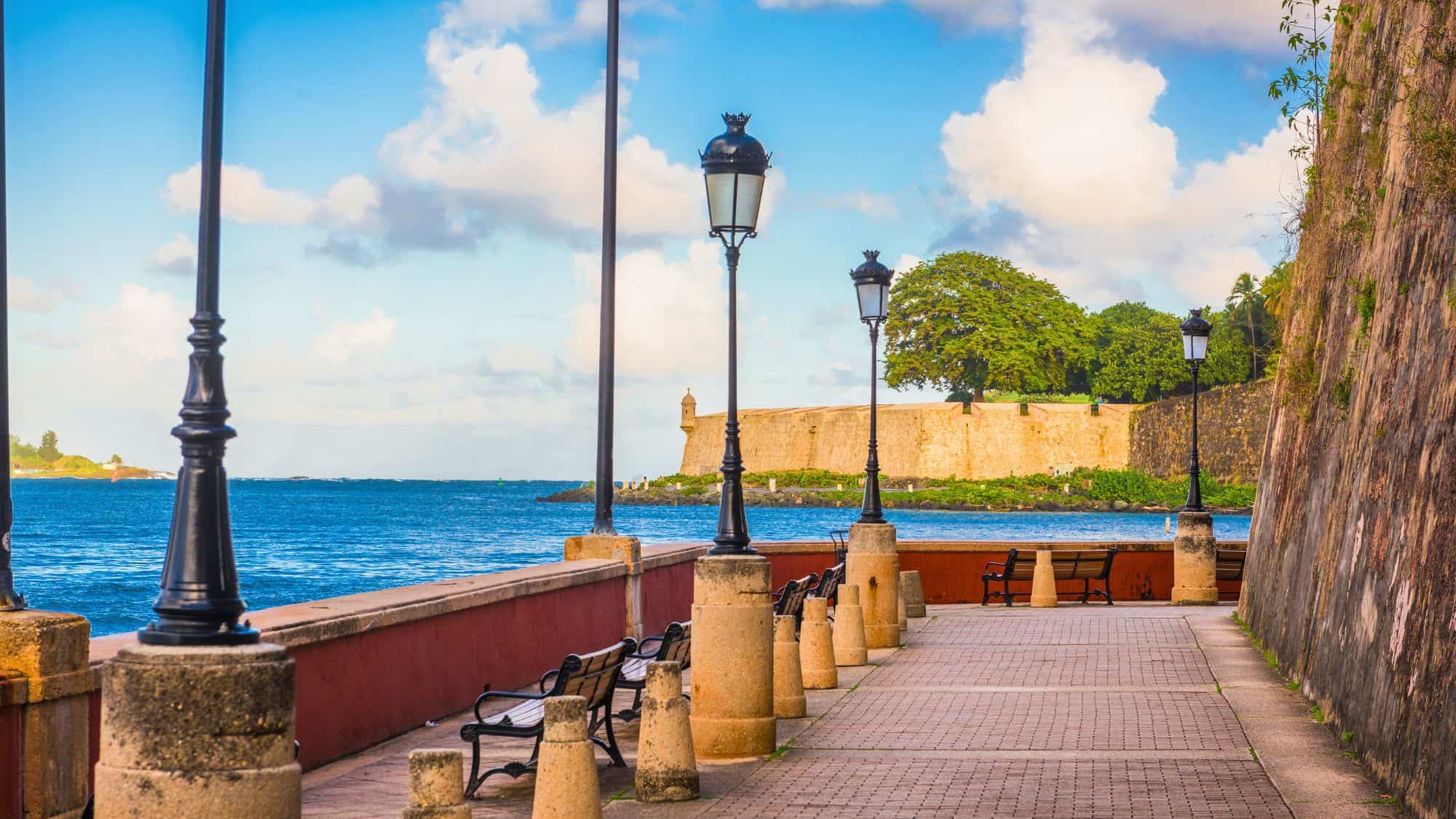 A cobblestone promenade with benches, lanterns, and ocean views runs alongside San Juan’s historic city walls.