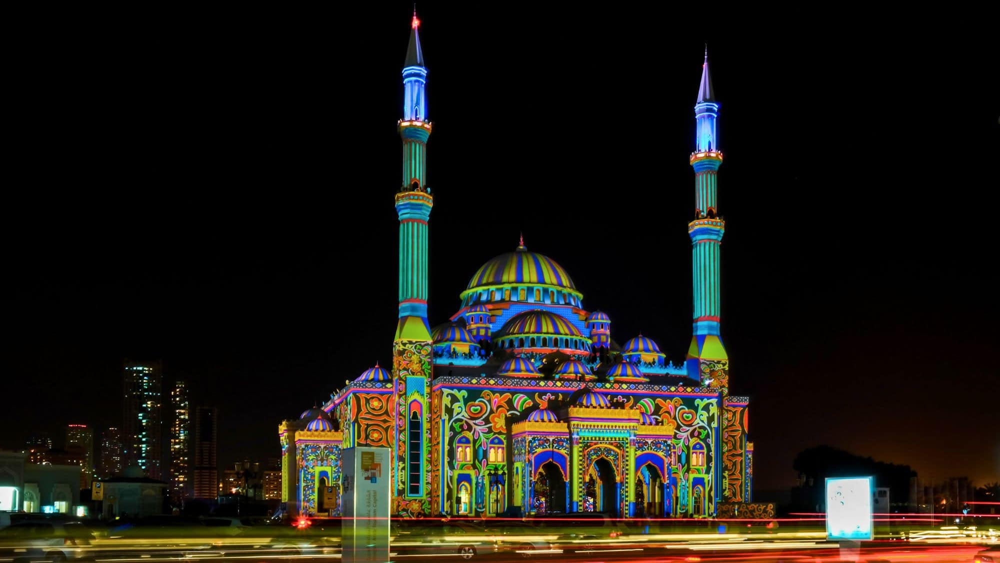 A grand mosque is transformed with bright neon patterns and colors projected across its domes and minarets.