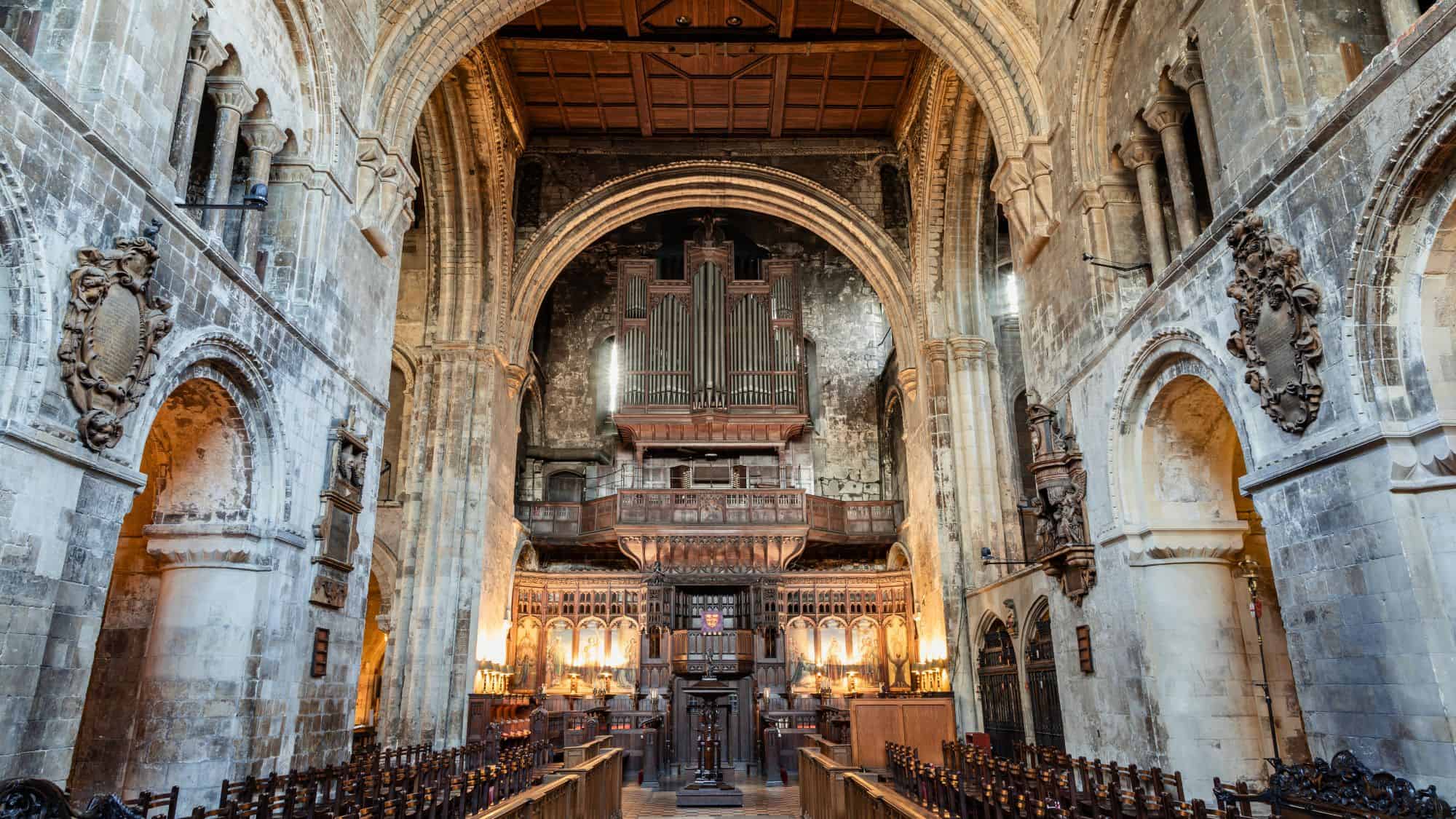 An atmospheric medieval church interior with high stone arches, an ornate wooden organ loft, and flickering candlelight.