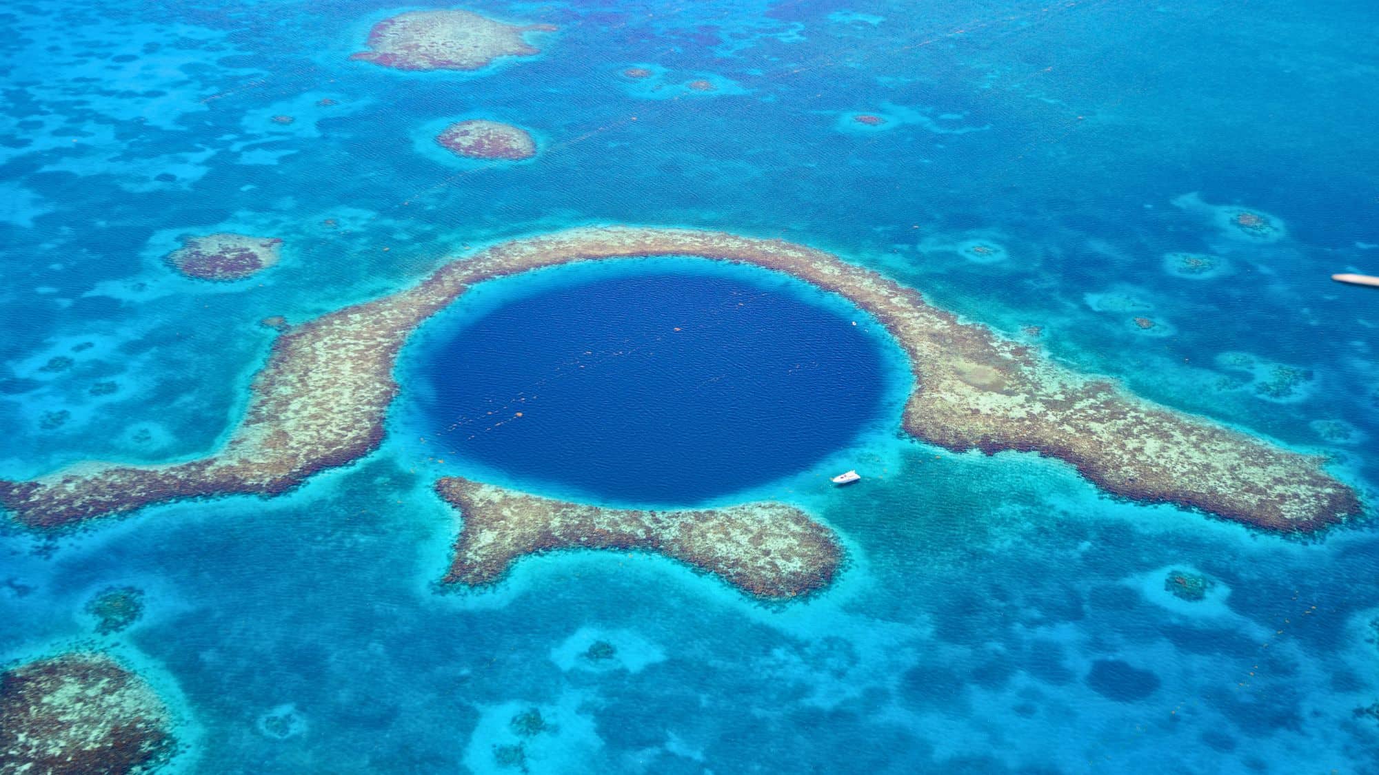 An aerial view of the famous deep blue circular sinkhole encircled by vibrant coral reef.