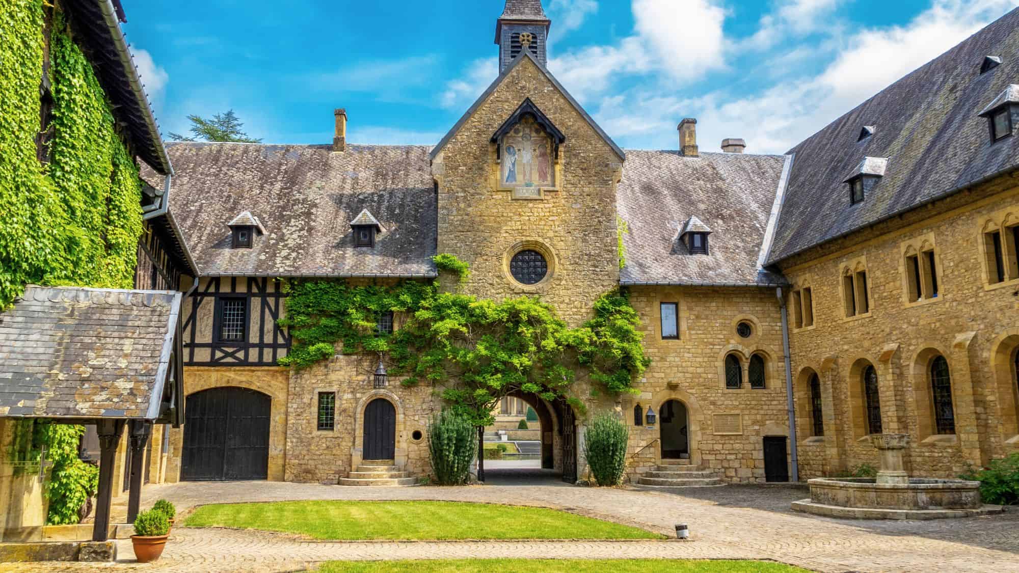 The ivy-covered stone walls and arched gateway of Orval Abbey surround a peaceful courtyard with a central fountain.