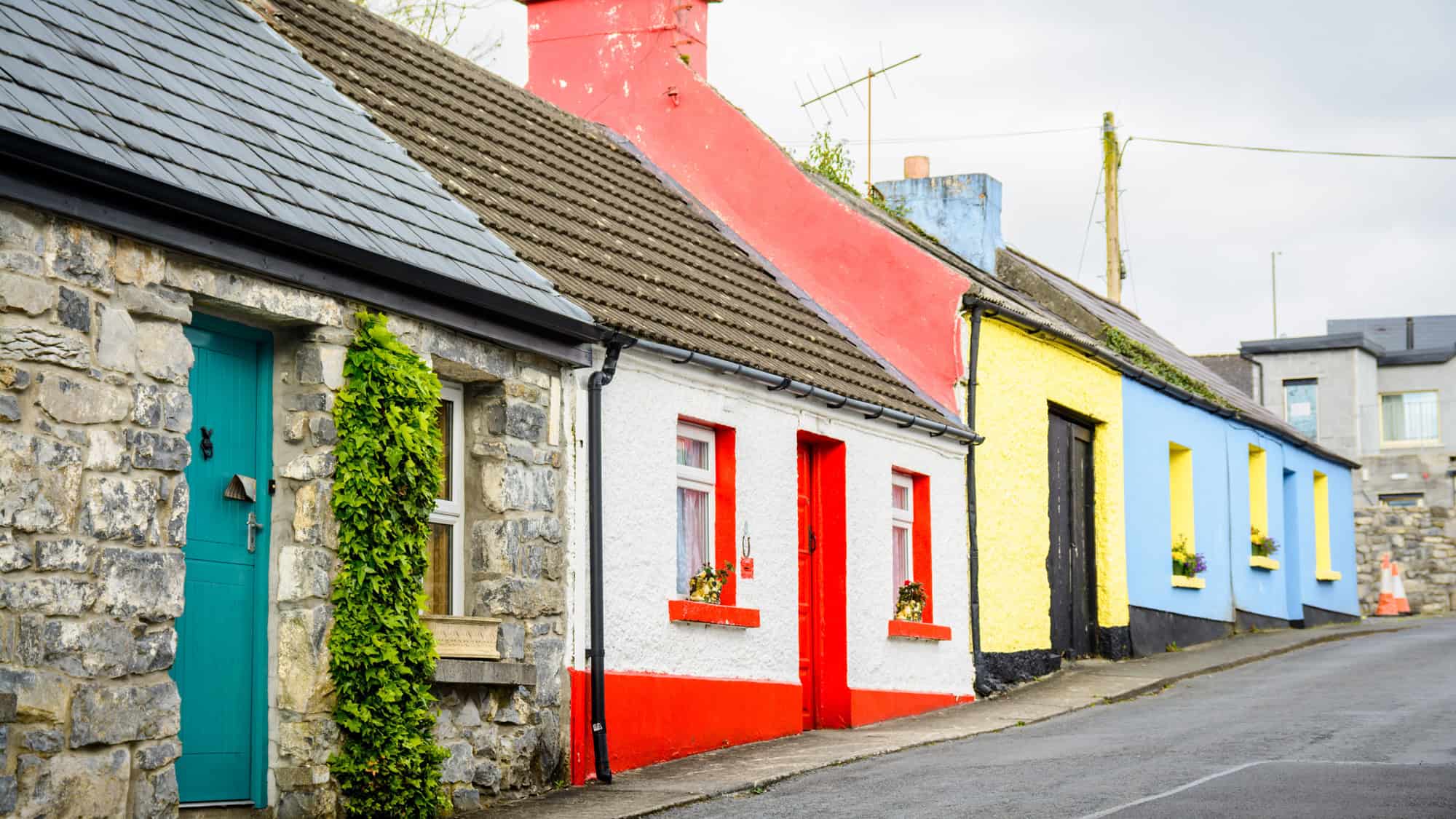 A row of small houses painted in bright red, yellow, and blue line a quiet street in Ireland.