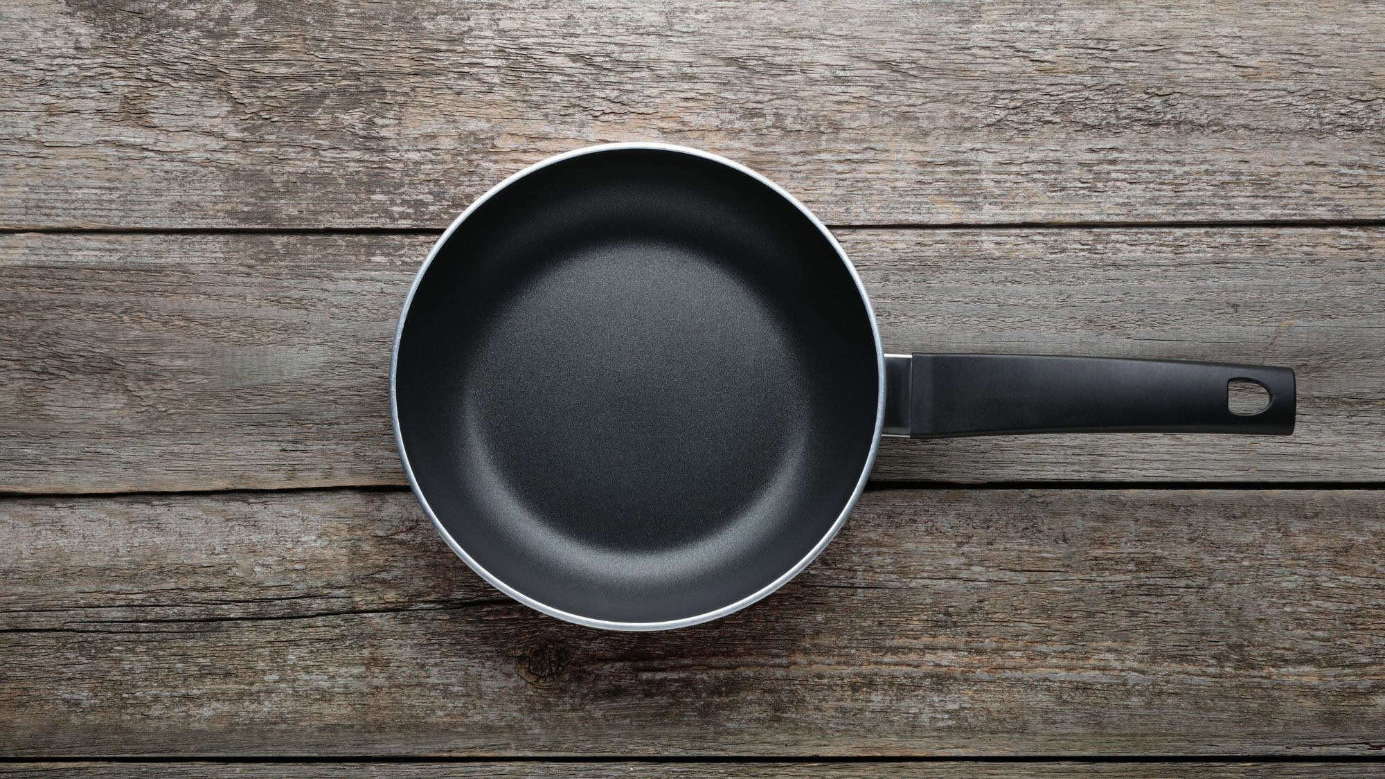 A black nonstick frying pan with a sleek handle rests on weathered wooden planks.