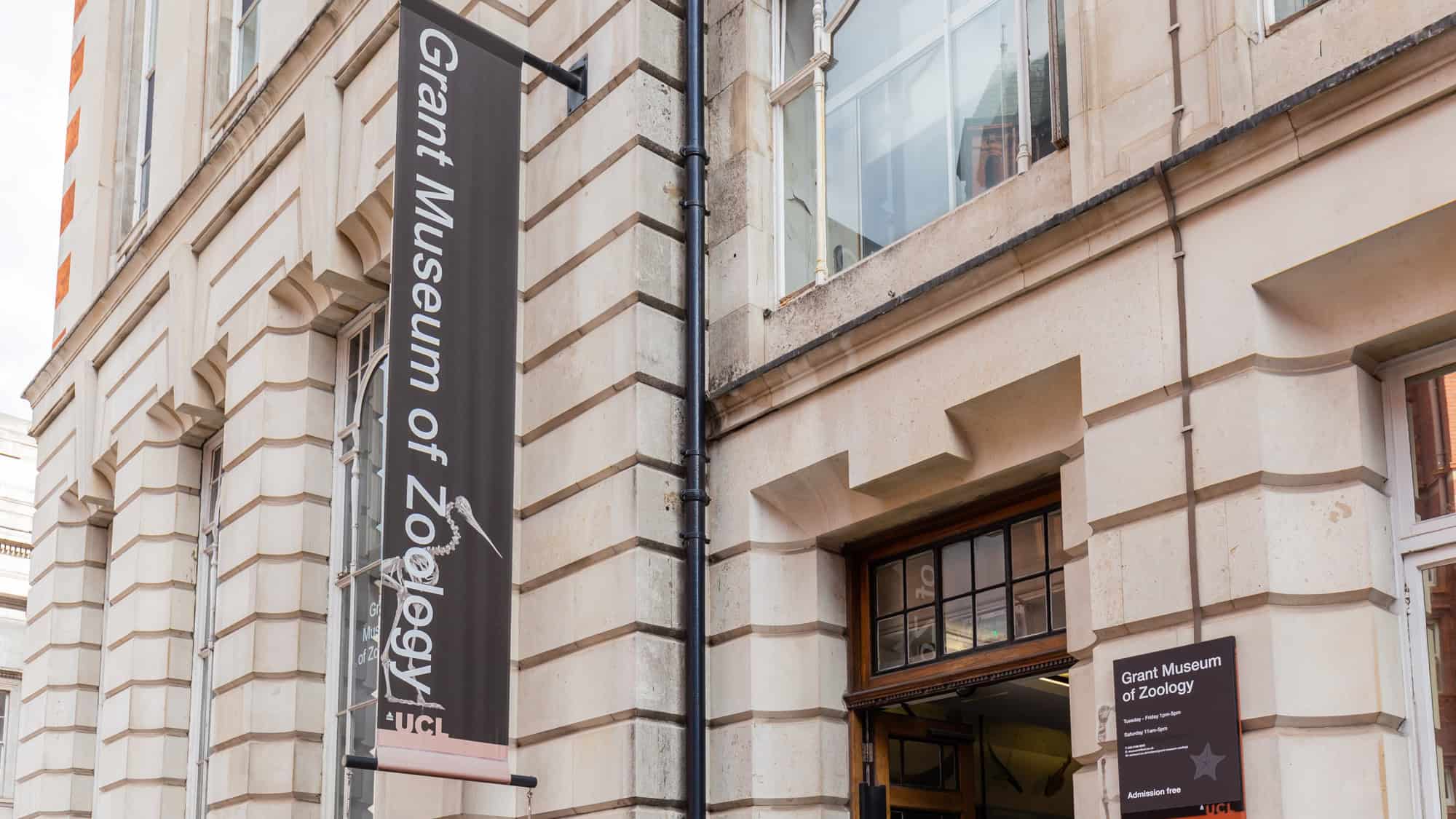 The exterior of the Grant Museum of Zoology shows its stone building with a vertical banner and sign by the doorway.