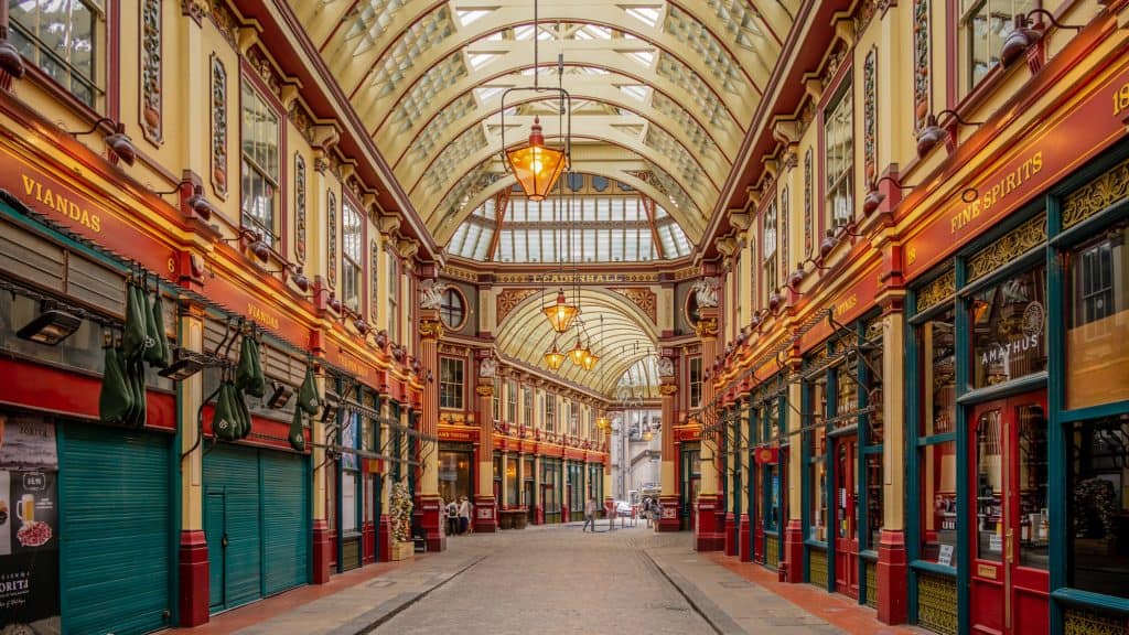 The ornate Victorian-style Leadenhall Market glows with warm lighting, colorful storefronts, and a vaulted glass roof.