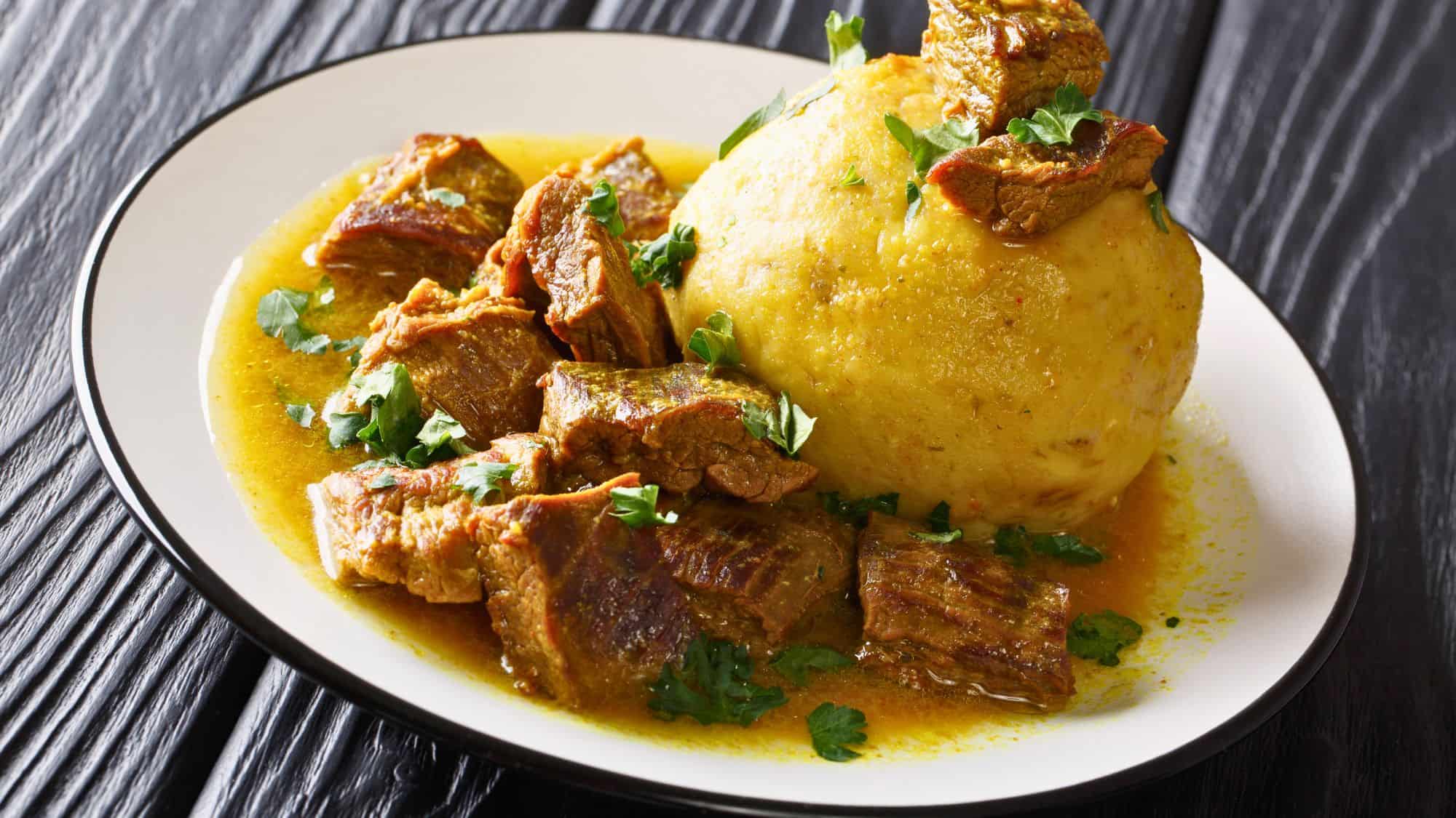 A plate of Puerto Rican mofongo served with tender chunks of stewed meat in a golden broth, garnished with fresh herbs.