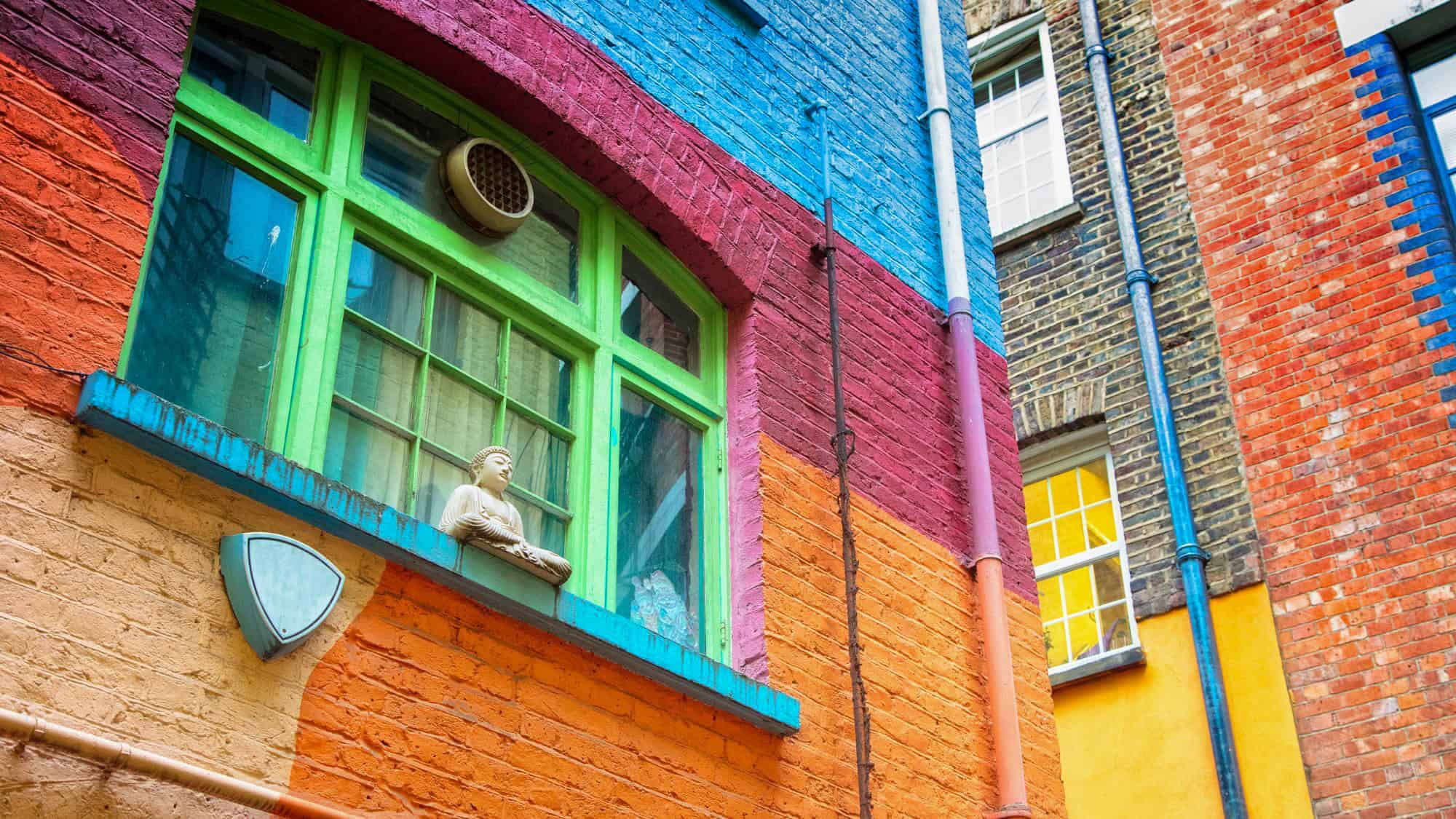 A vibrant painted wall in shades of orange, red, and blue features a green-trimmed window with a small Buddha statue on the sill.