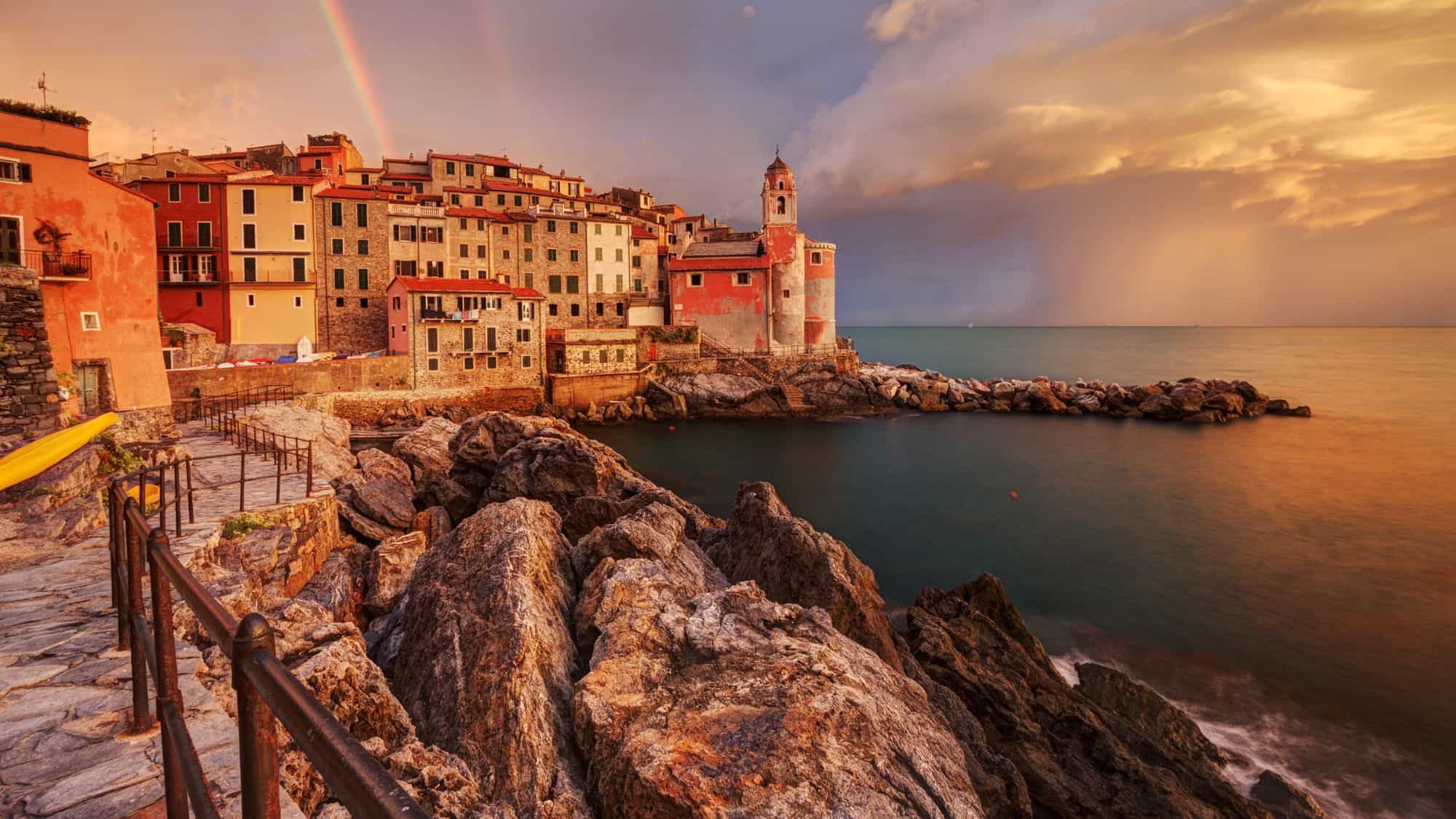 A rainbow arcs above the pastel-colored cliffside village of Tellaro as it overlooks the sea at sunset.