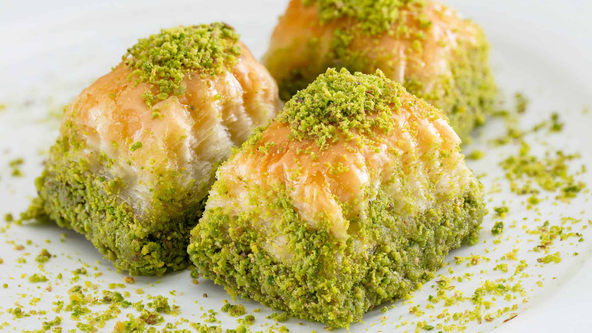 Golden layers of flaky pastry are generously coated with crushed green pistachios.
