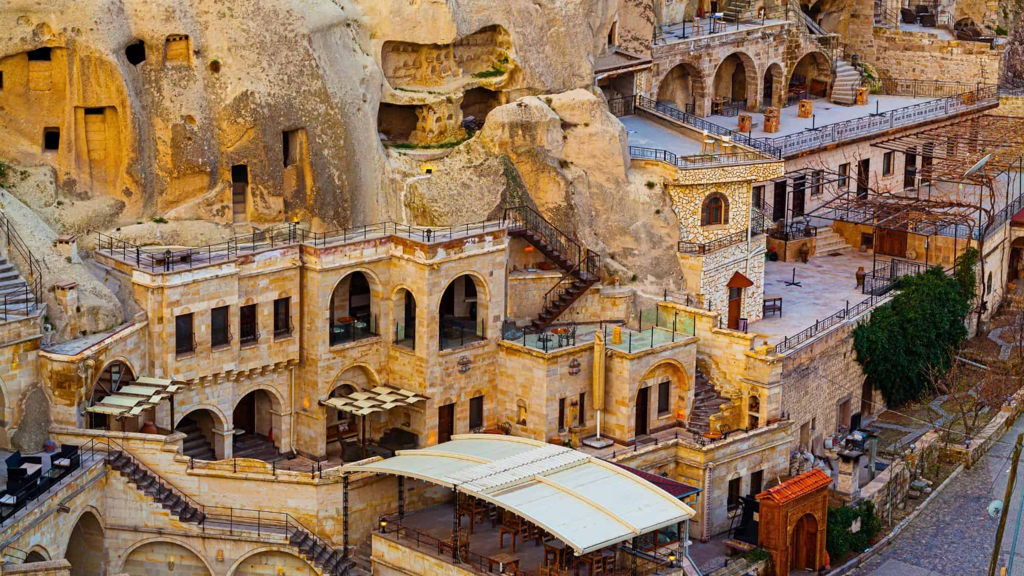 A hillside cave hotel in Cappadocia, Turkey, features arched balconies and terraces built into soft volcanic rock formations, blending ancient architecture with modern hospitality.