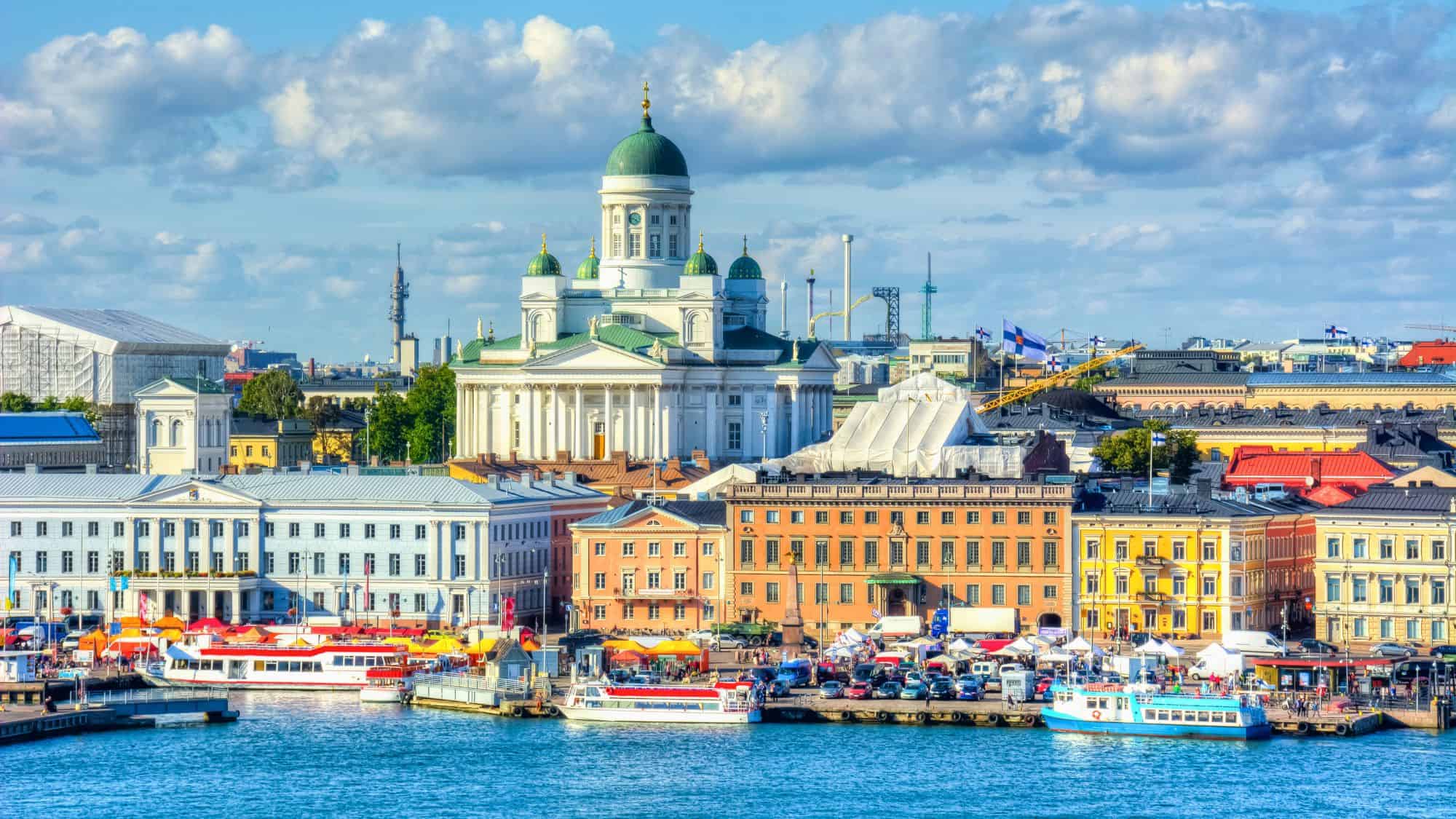 The Helsinki Cathedral with its green domes rises above colorful historic buildings and a busy waterfront market.