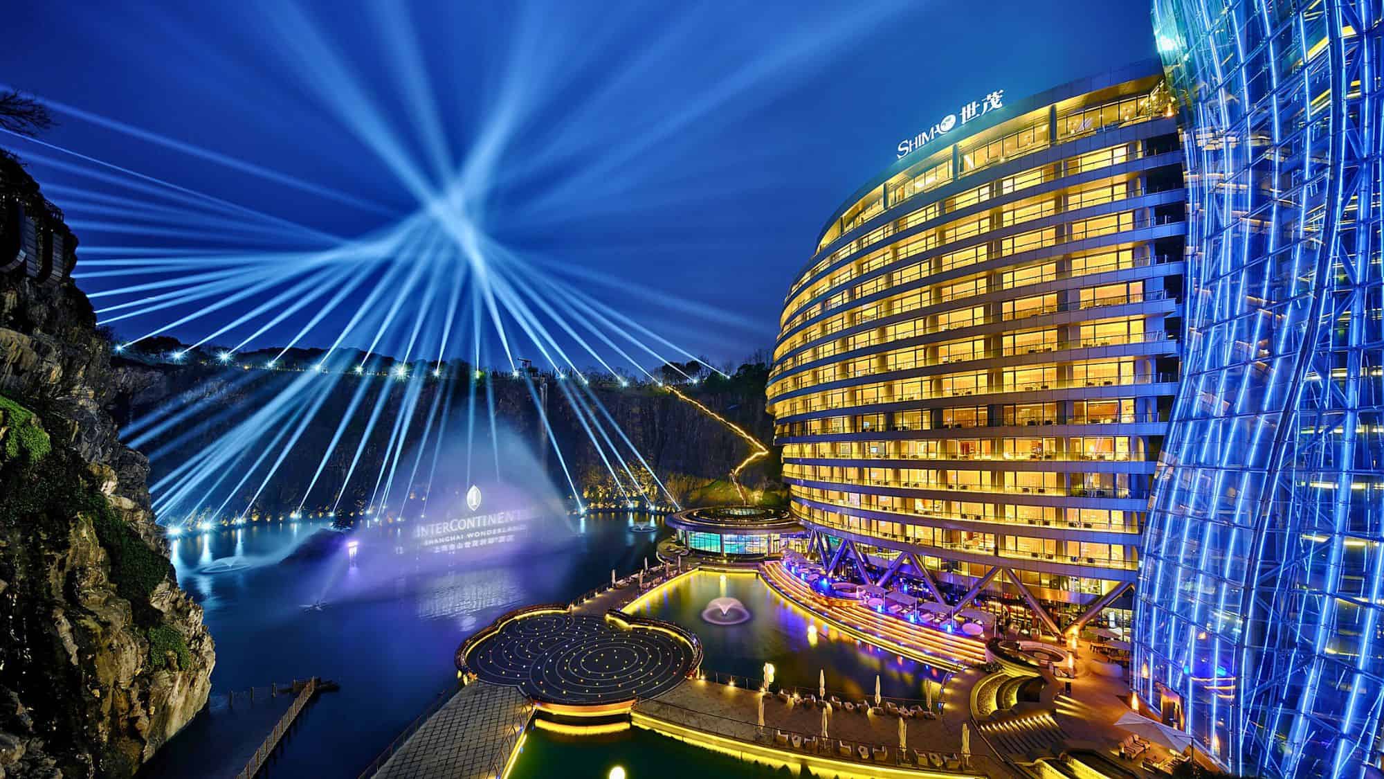 The InterContinental Shanghai Wonderland glows in gold and blue within an abandoned quarry, with dramatic laser light beams fanning out over the water and cliffs.