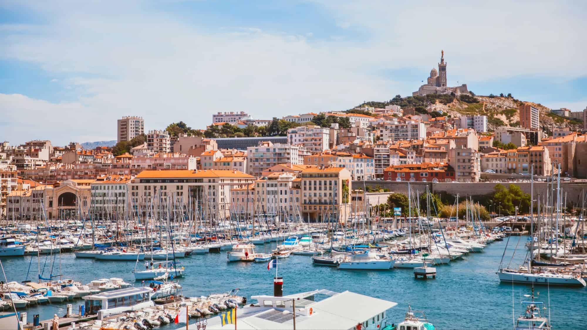 Boats fill the Old Port of Marseille with terracotta-roofed buildings and Notre-Dame de la Garde basilica perched on the hill.