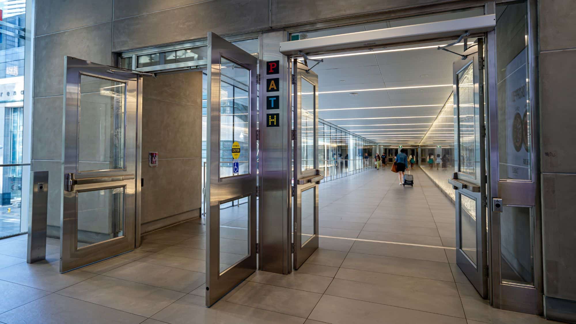 Brightly lit entrance to Toronto’s PATH system shows automatic doors opening into a modern underground pedestrian tunnel with tile flooring and glass walls.