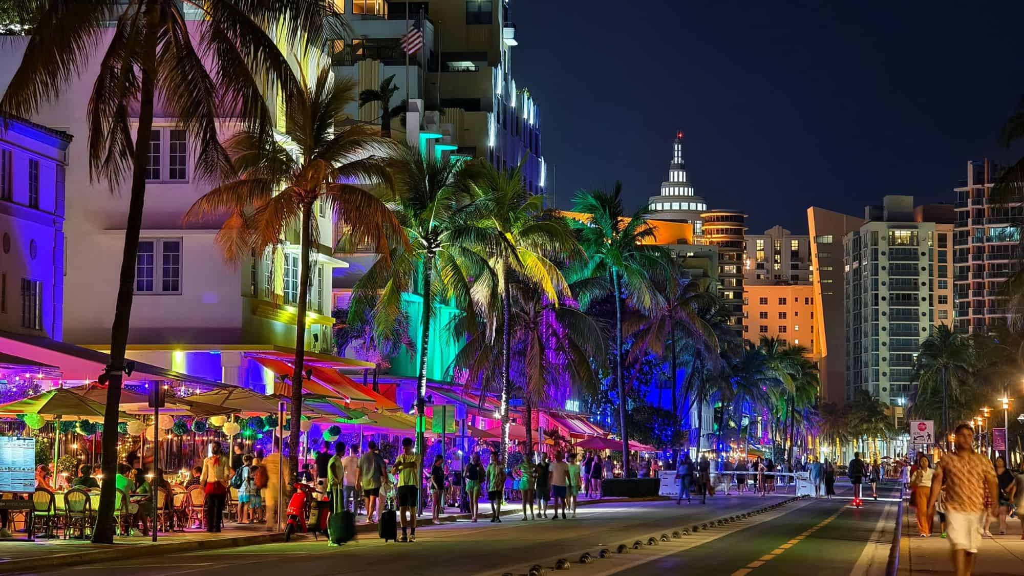 Miami Beach’s Ocean Drive comes alive at night with neon-lit Art Deco buildings, colorful patio umbrellas, palm trees, and crowds enjoying the nightlife.