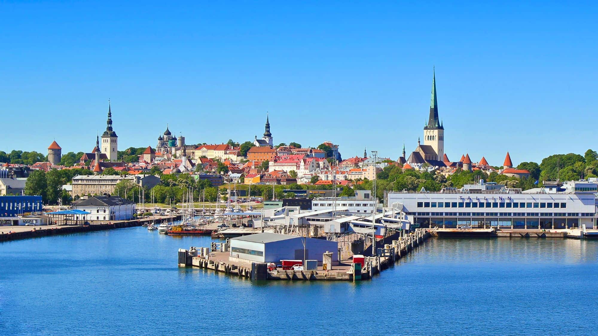 The medieval skyline of Tallinn, Estonia with church spires and red-roofed towers overlooks a modern waterfront and marina.