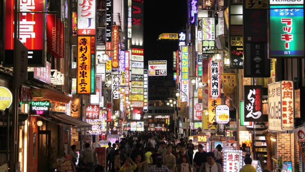 A packed pedestrian street in Tokyo’s Kabukicho district is lit by countless signs in Japanese advertising restaurants, bars, and entertainment venues.