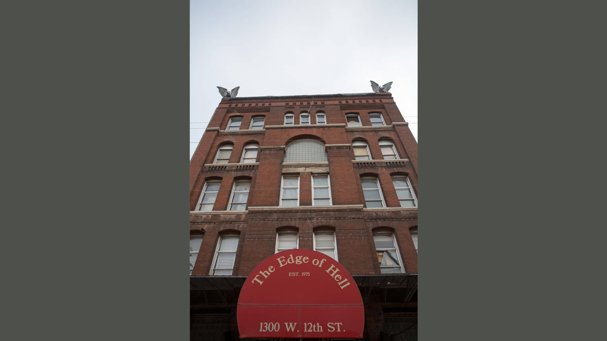 A tall brick building with gothic touches features a red awning labeled “The Edge of Hell” above its entrance, promoting a haunted attraction in Kansas City.