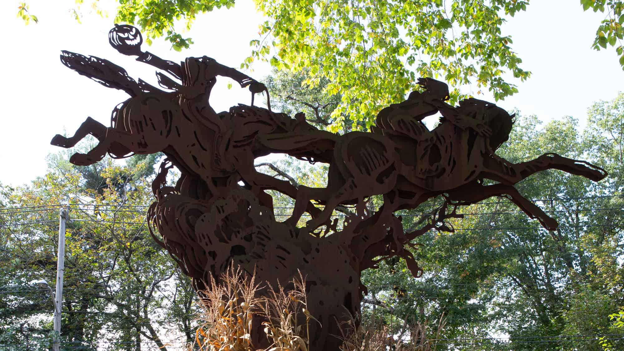 A dramatic rusted metal sculpture shows the Headless Horseman wielding a jack-o'-lantern while chasing Ichabod Crane through the woods on horseback.