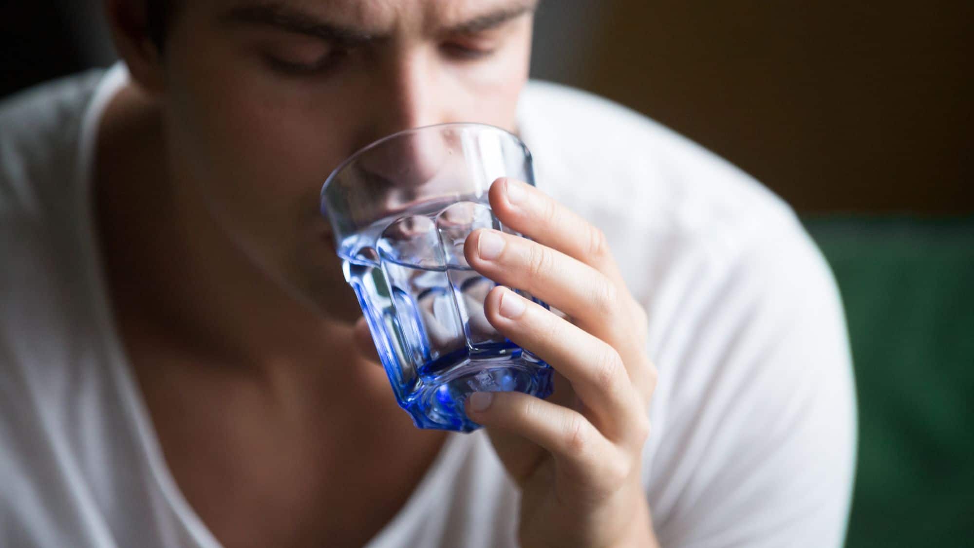 A close-up of a man holding a glass of water to his lips, preparing to take a sip.