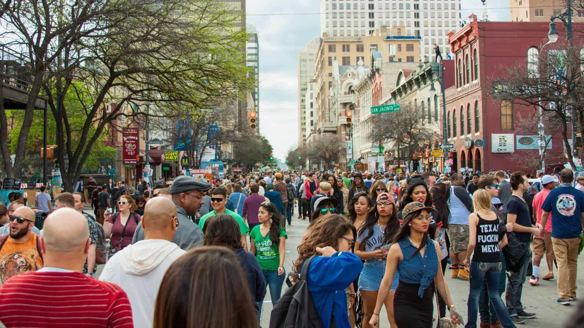A bustling crowd fills Austin’s famous 6th Street during a lively festival, surrounded by bars, music venues, and historic downtown buildings.