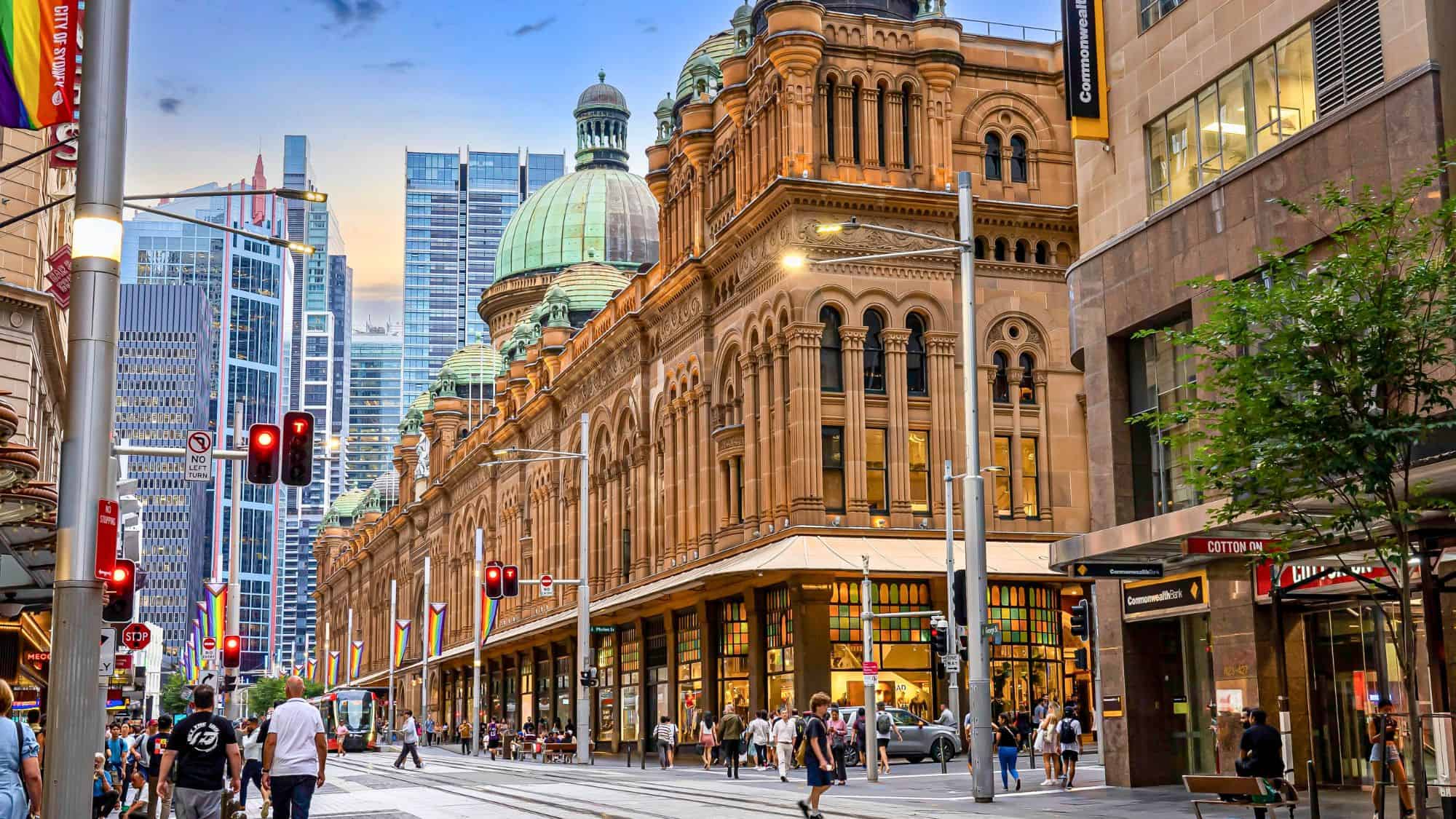 The historic Queen Victoria Building in Sydney stands out with its sandstone façade and green domes, surrounded by modern skyscrapers and a busy pedestrian street.