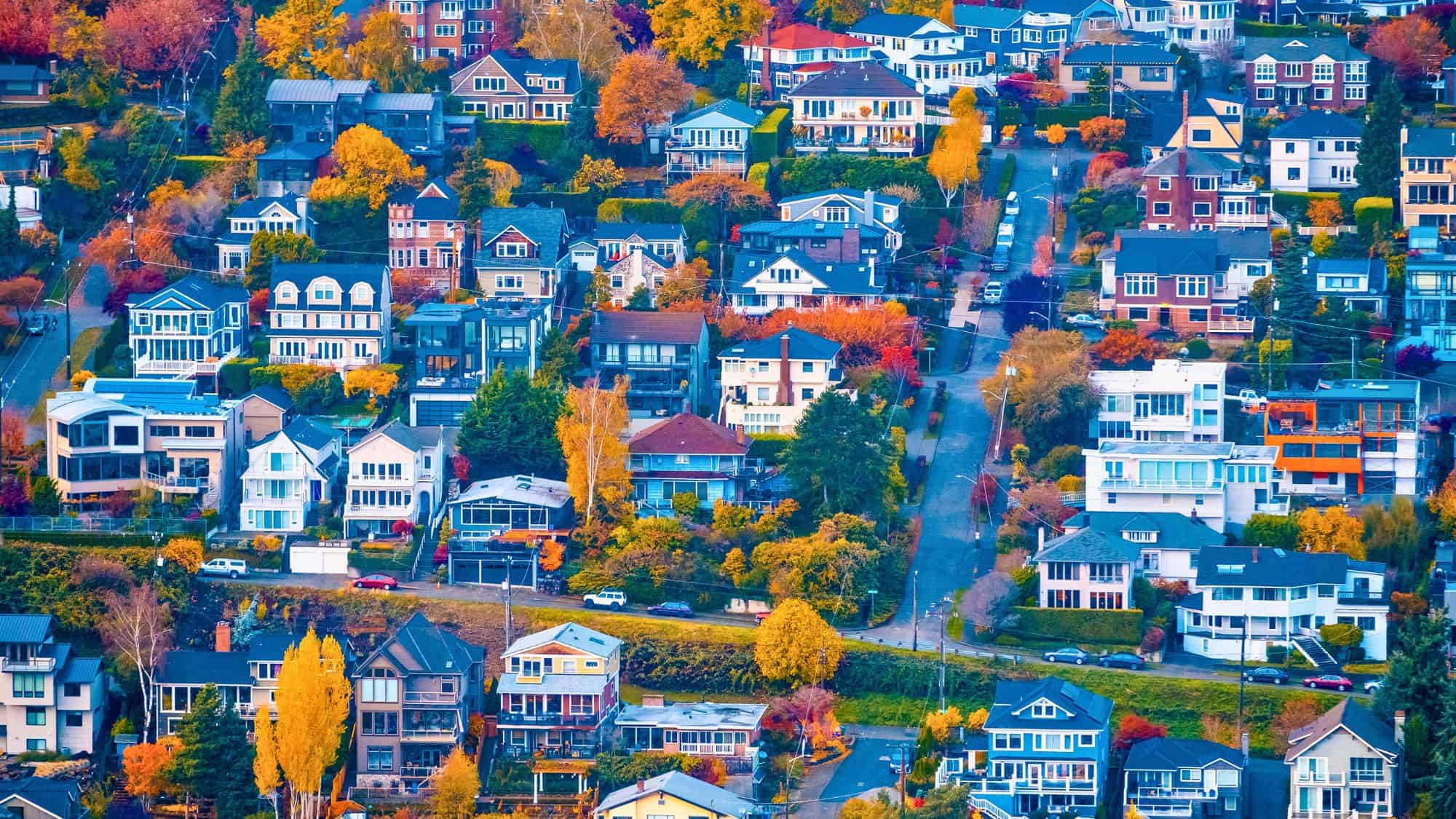 A dense hillside neighborhood is filled with charming houses in a rainbow of colors, surrounded by vivid fall foliage in golden, orange, and red tones.