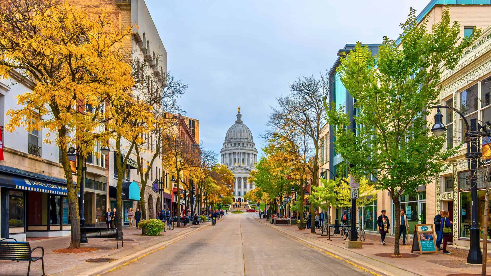 Visitors stroll through Chicago’s Millennium Park in fall, with the reflective Bean sculpture and vibrant red-orange trees standing out against surrounding skyscrapers.