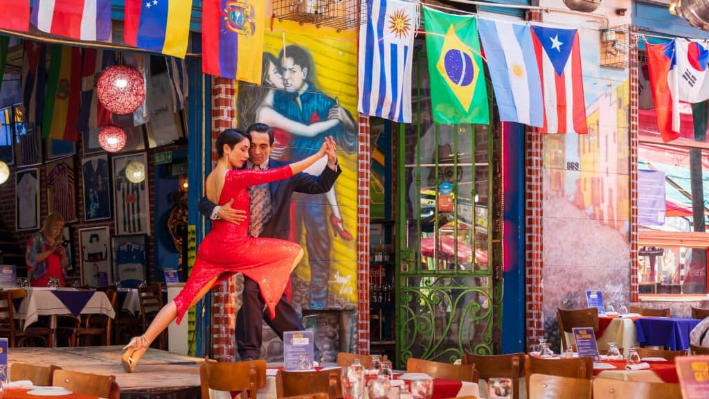 A passionate tango duo performs in a vibrant restaurant adorned with colorful flags and murals in Buenos Aires, capturing the city’s rich dance and cultural heritage.