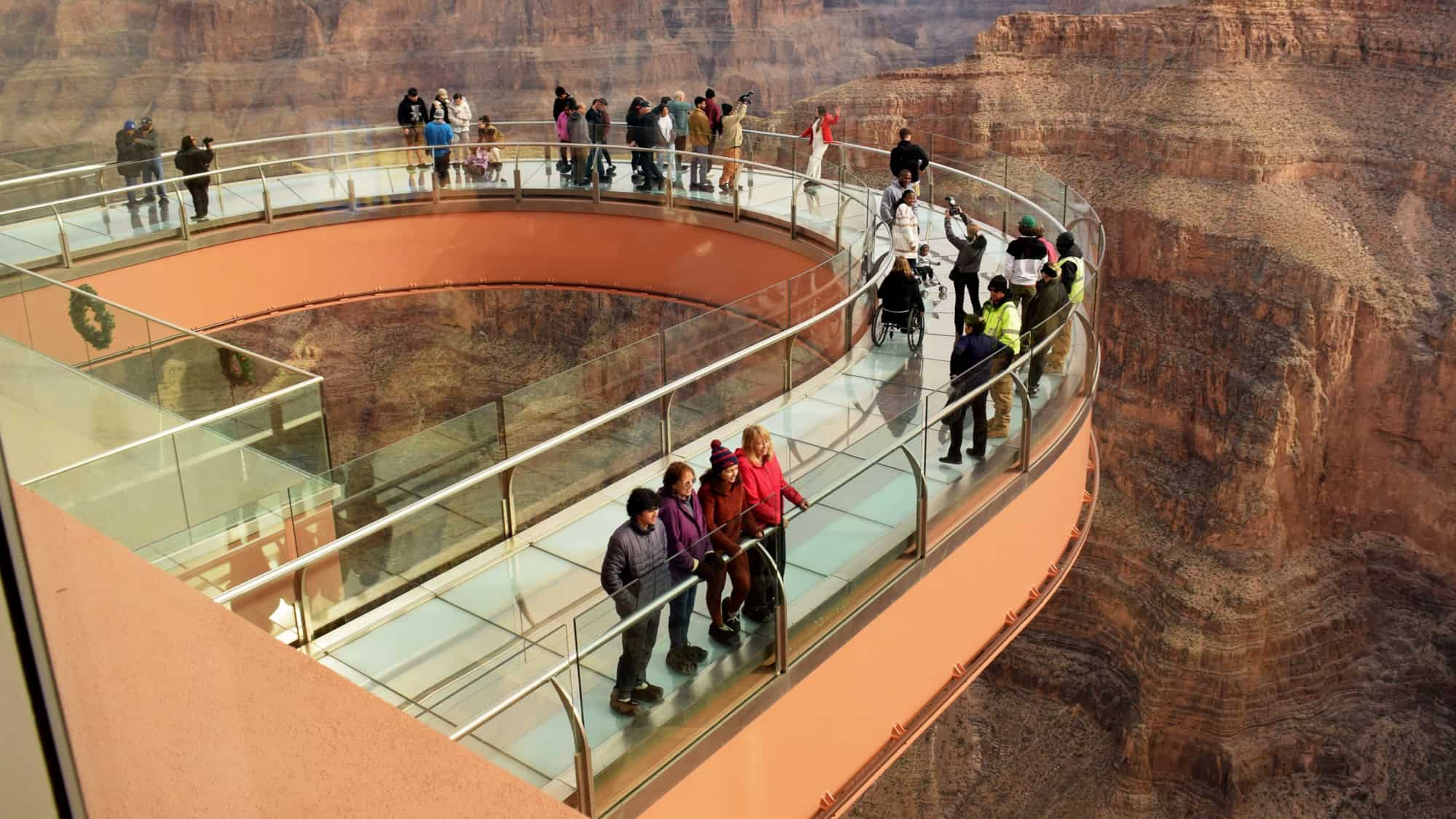 Visitors stroll along the glass-bottomed Grand Canyon Skywalk, a horseshoe-shaped platform extending over the canyon’s edge, offering dramatic views straight down into the red rock cliffs.
