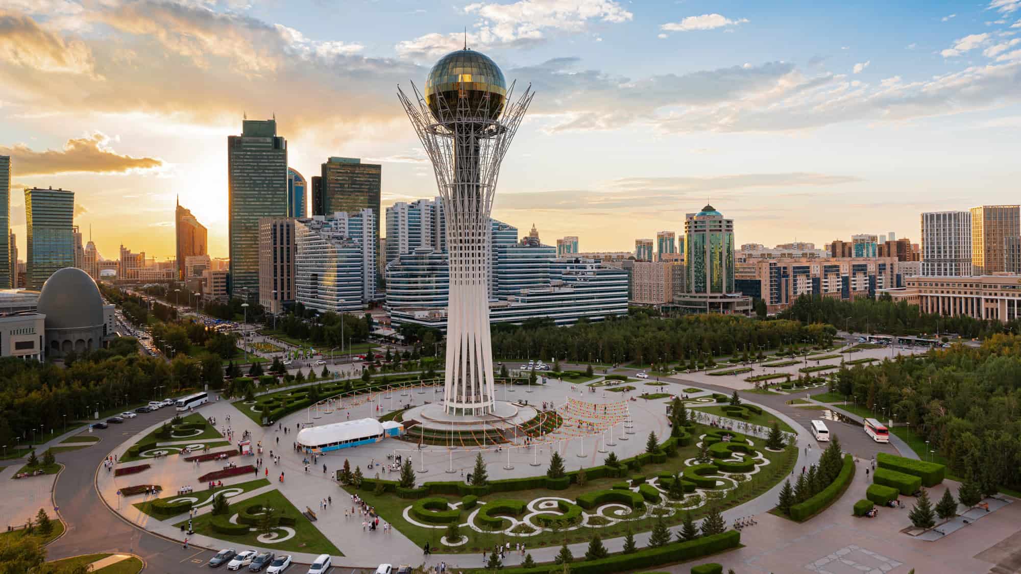 The futuristic Bayterek Tower rises in the center of Nur-Sultan’s skyline, surrounded by manicured gardens and modern high-rises at sunset.